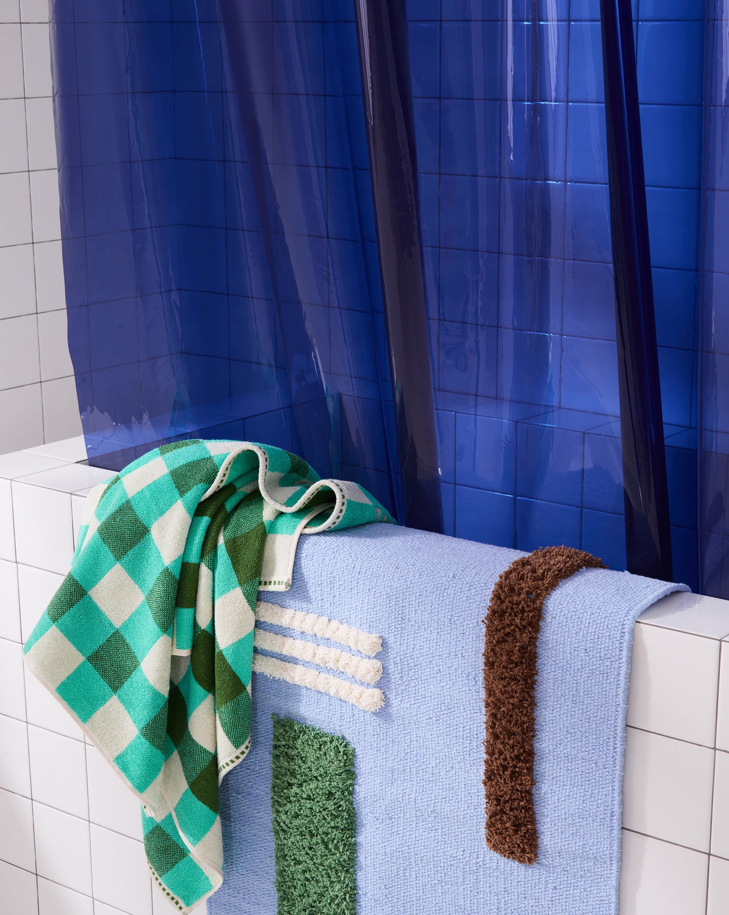 Sun shower navy curtain hanging in white tiled bathtub styled with Atlantic Reyes rug and tam bath sheet.