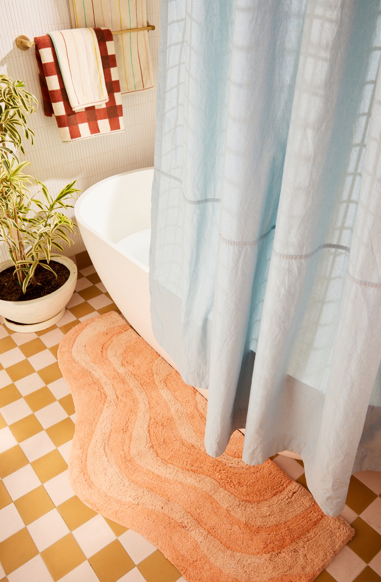 Bathroom with a bathtub, shower curtain, bath mat, and plants on a checkered floor.