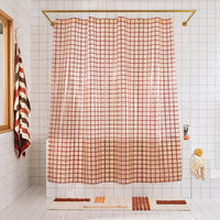 Checkered shower curtain in a bathroom with tiled walls and a bath mat on the floor.