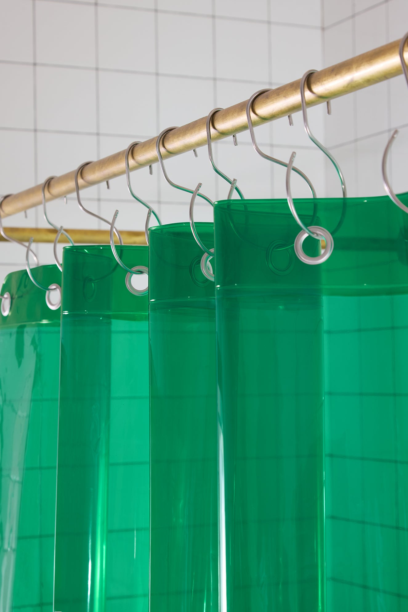 Green shower curtain with hooks on a gold rod against a tiled wall.
