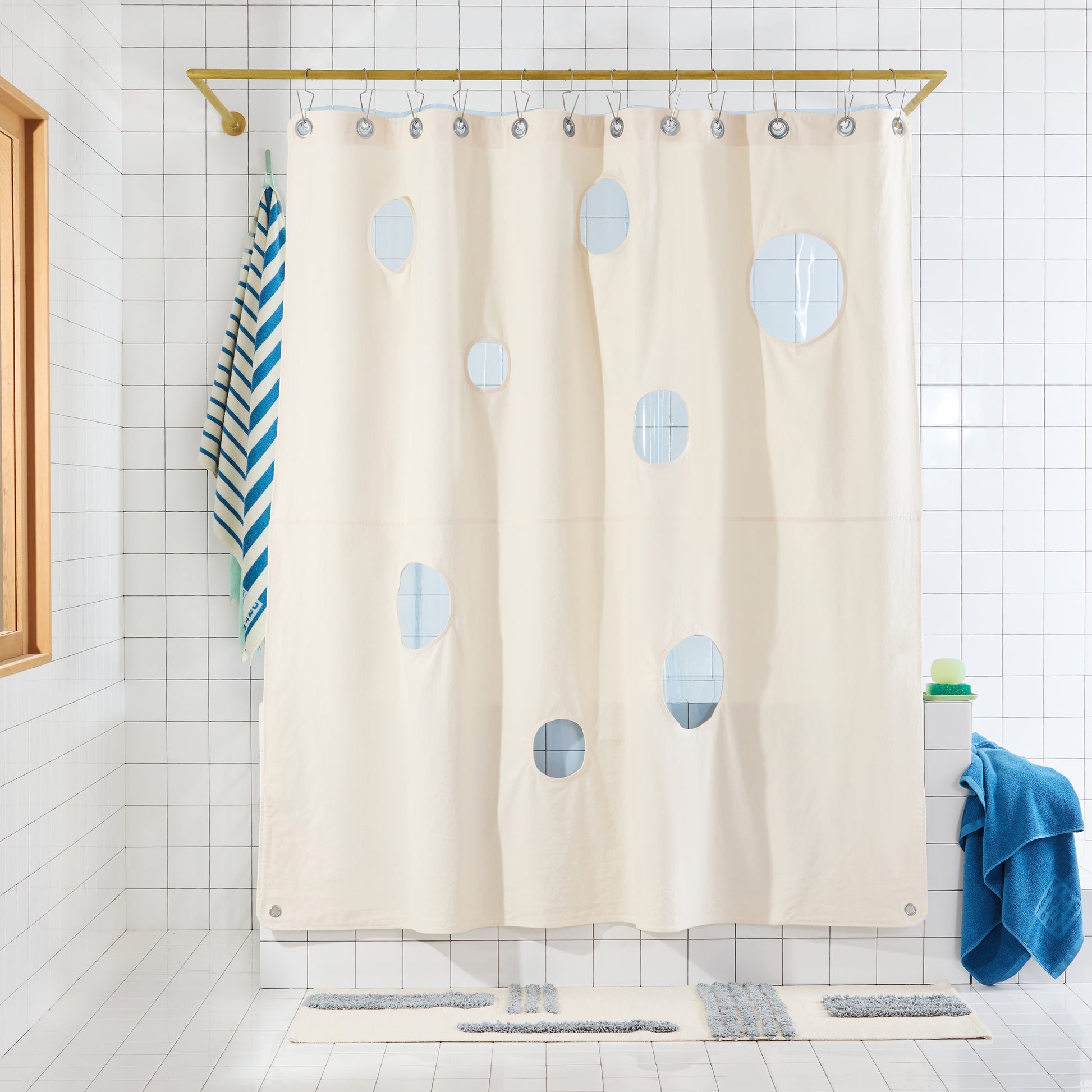Natural colored shower curtain with circular cut-outs and blue sun shwoer layered behind it. 