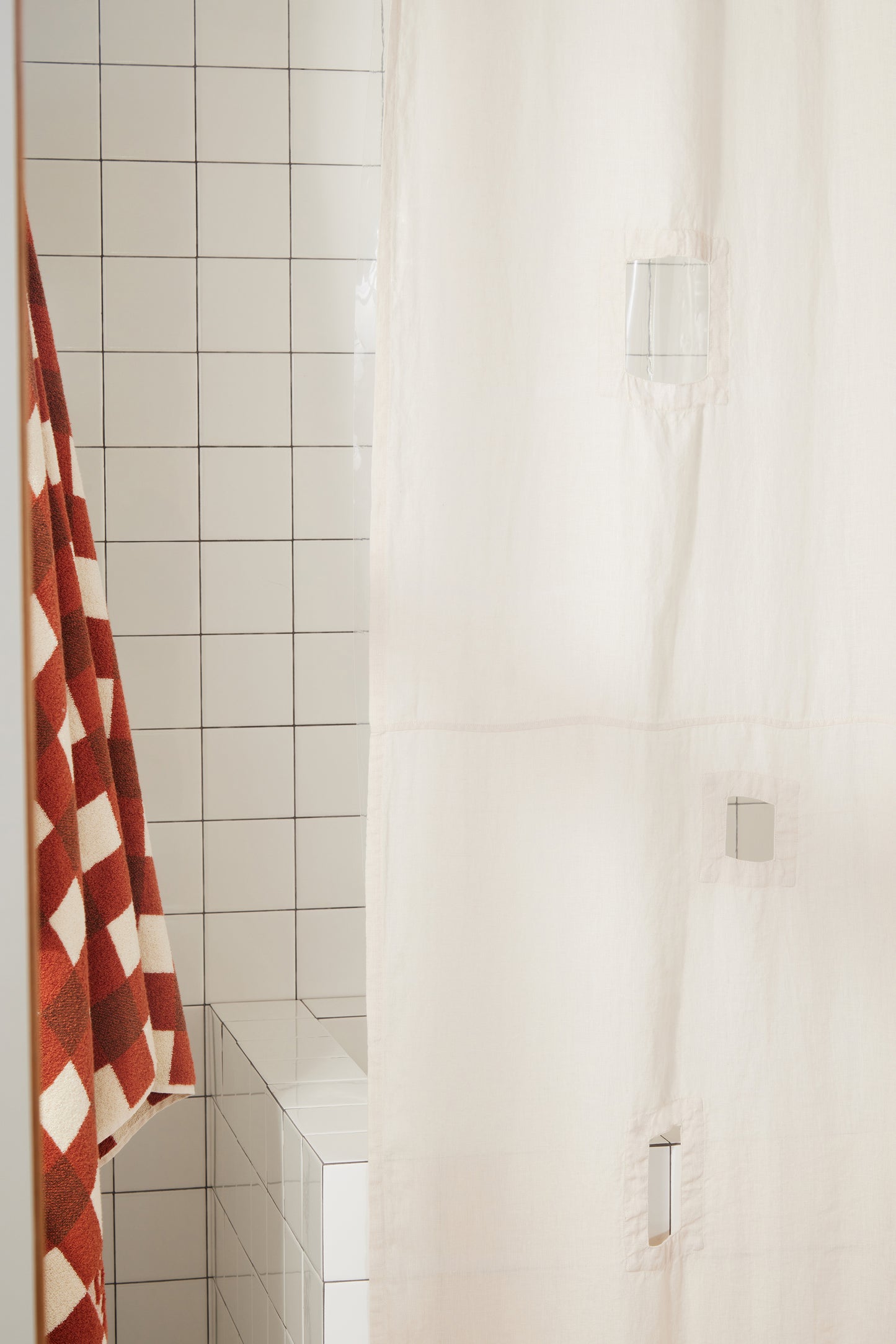 Cream shower curtain with tiled wall, red and white patterned towel.