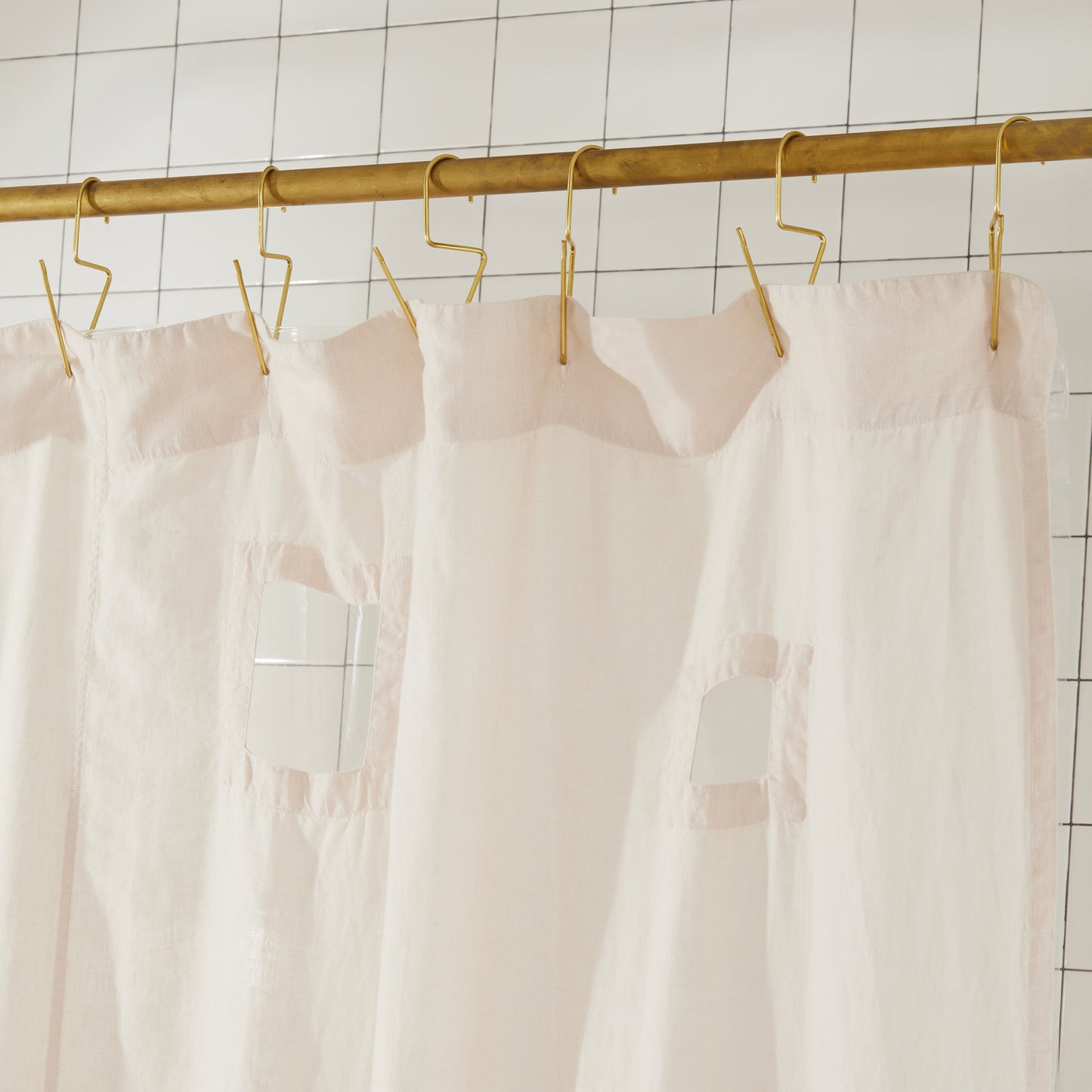 
Cream shower curtain with cut outs hanging on a gold rod against a tiled wall
