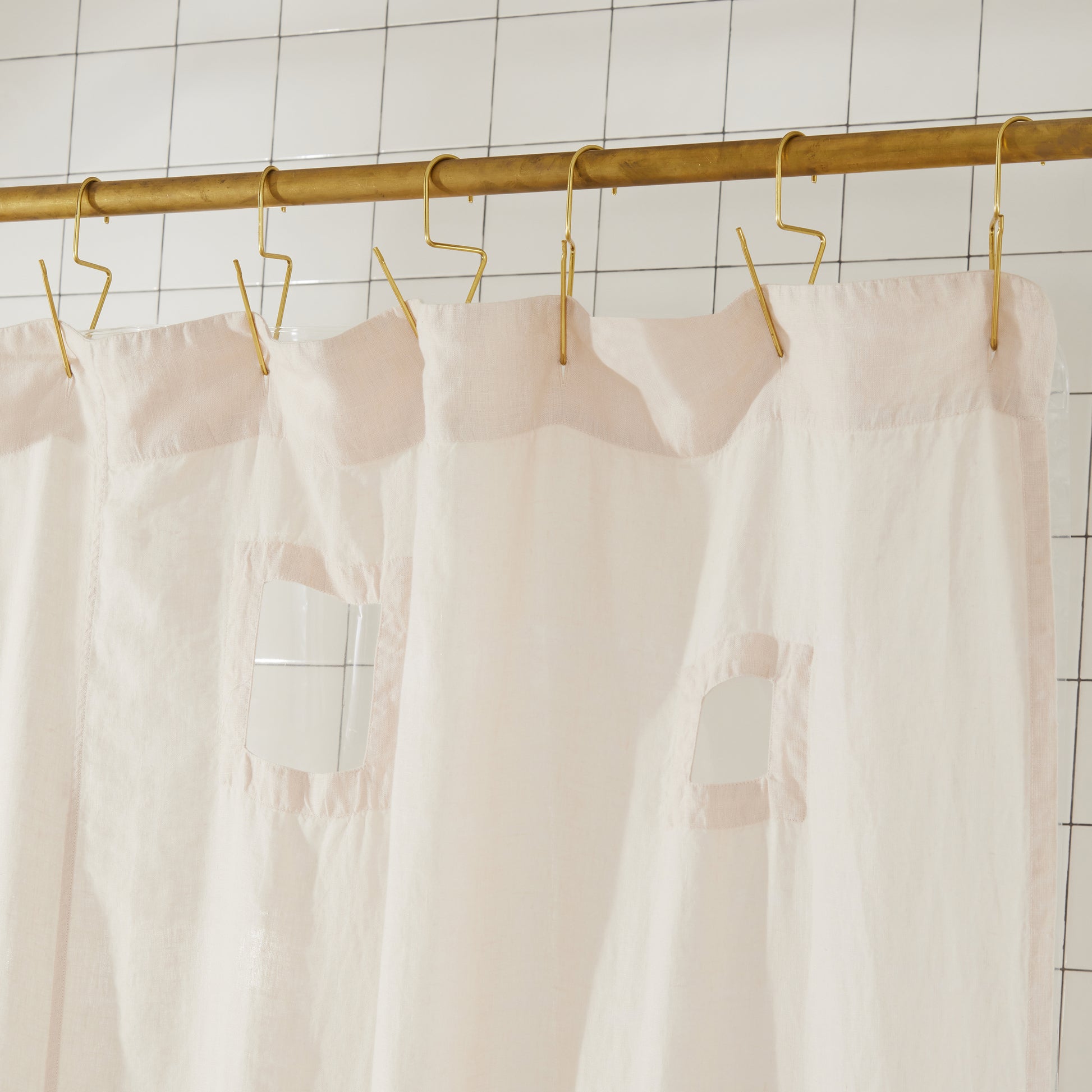 
Cream shower curtain with cut outs hanging on a gold rod against a tiled wall