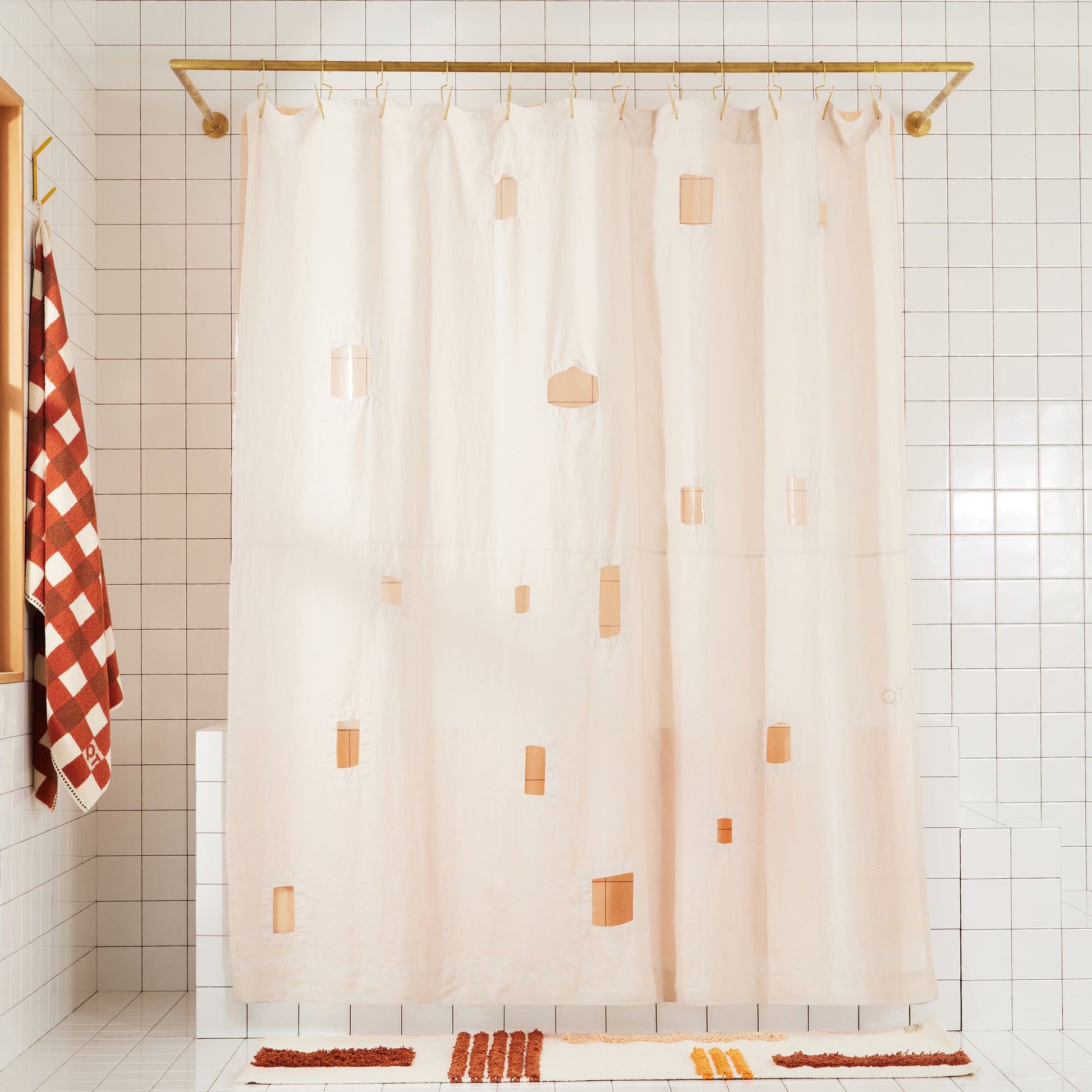 cream colored shower curtain with varying cut out squares and rectangles with peach colored transparent shower curtain hanging behind it in a white bathroom. 