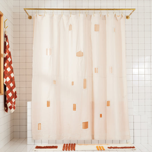 cream colored shower curtain with varying cut out squares and rectangles with peach colored transparent shower curtain hanging behind it in a white bathroom. 