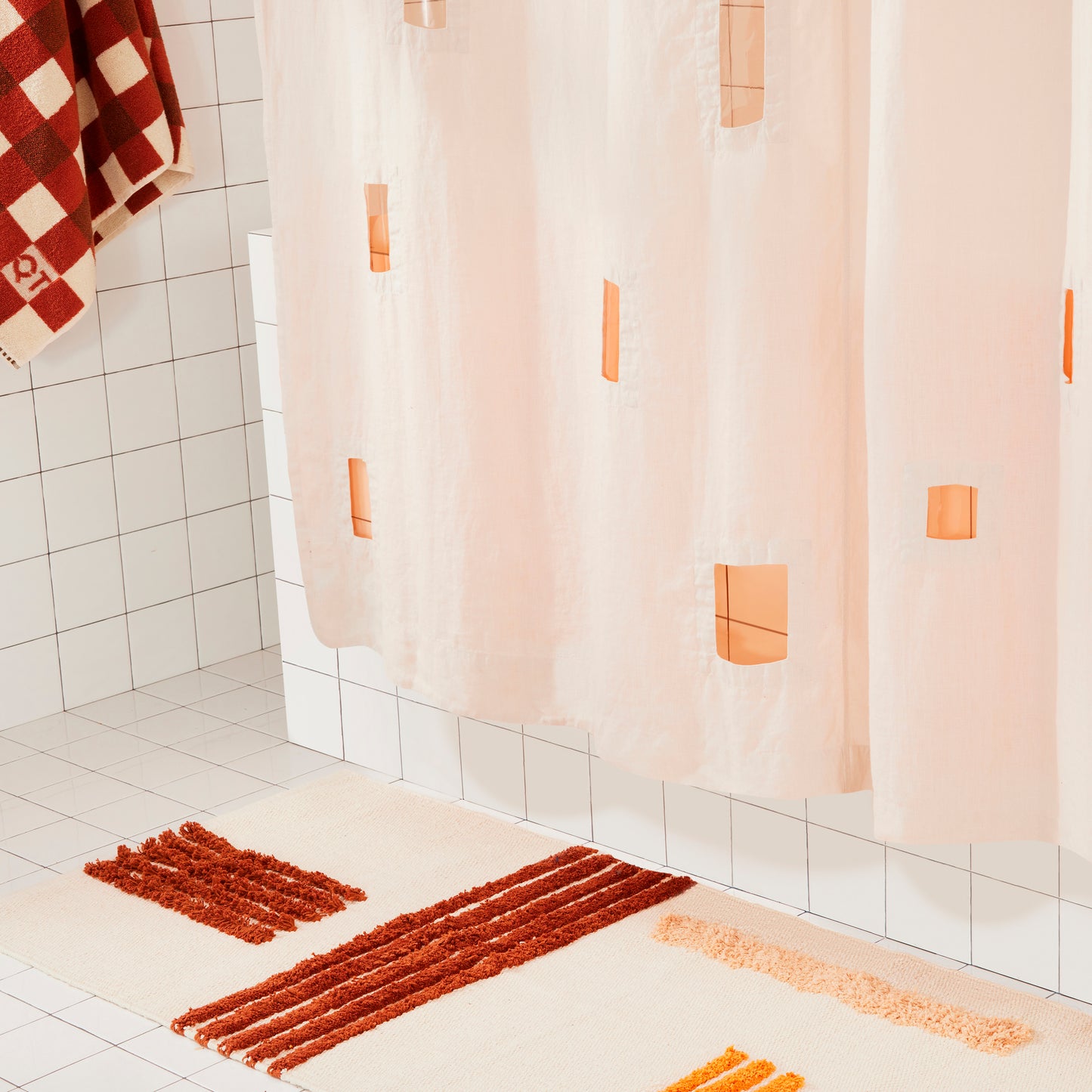 Cream shower curtain with geometric cut outs in a bathroom setting wtih striped rug. 