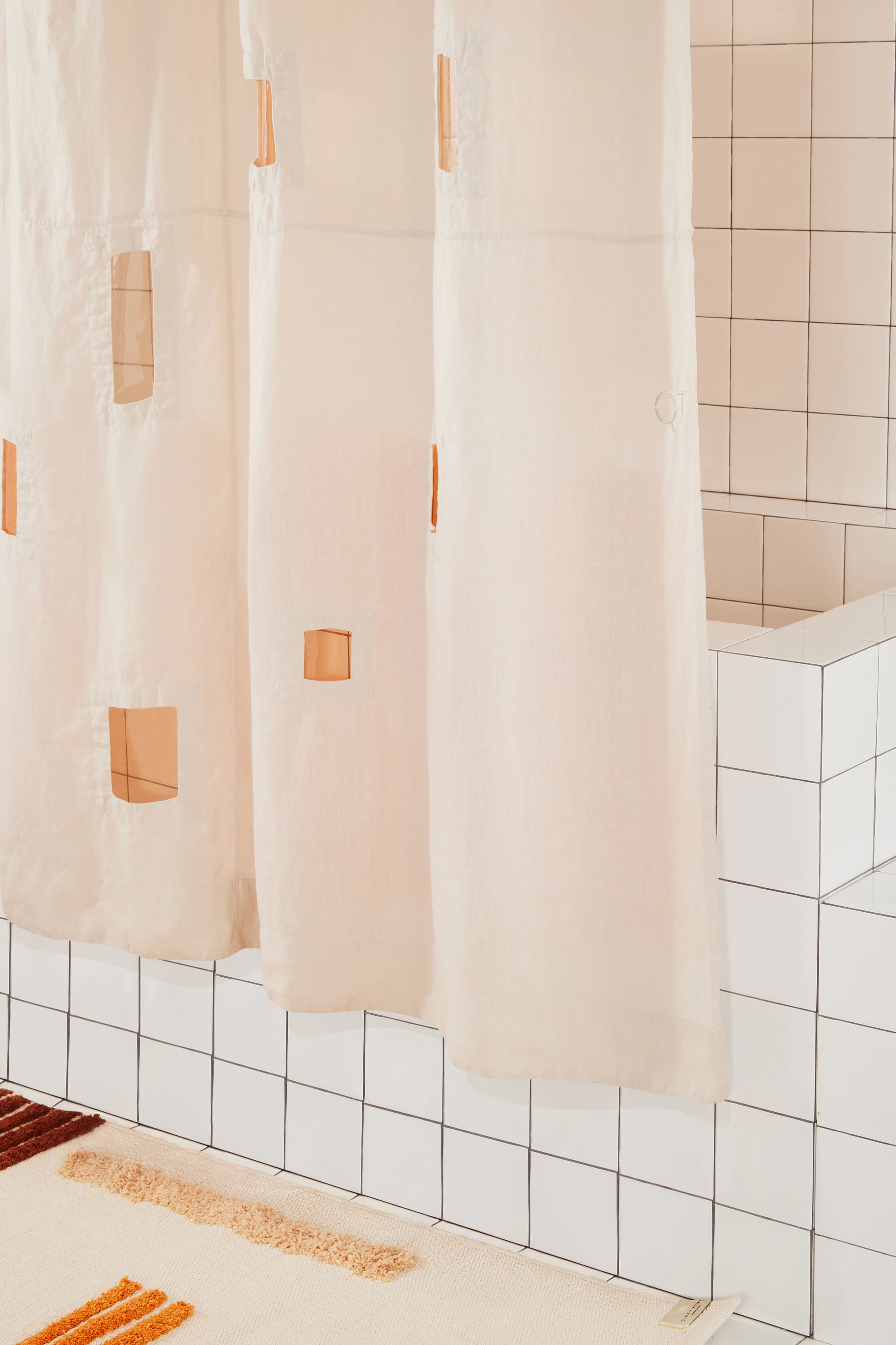 Beige shower curtain with  cut out accents in a tiled bathroom