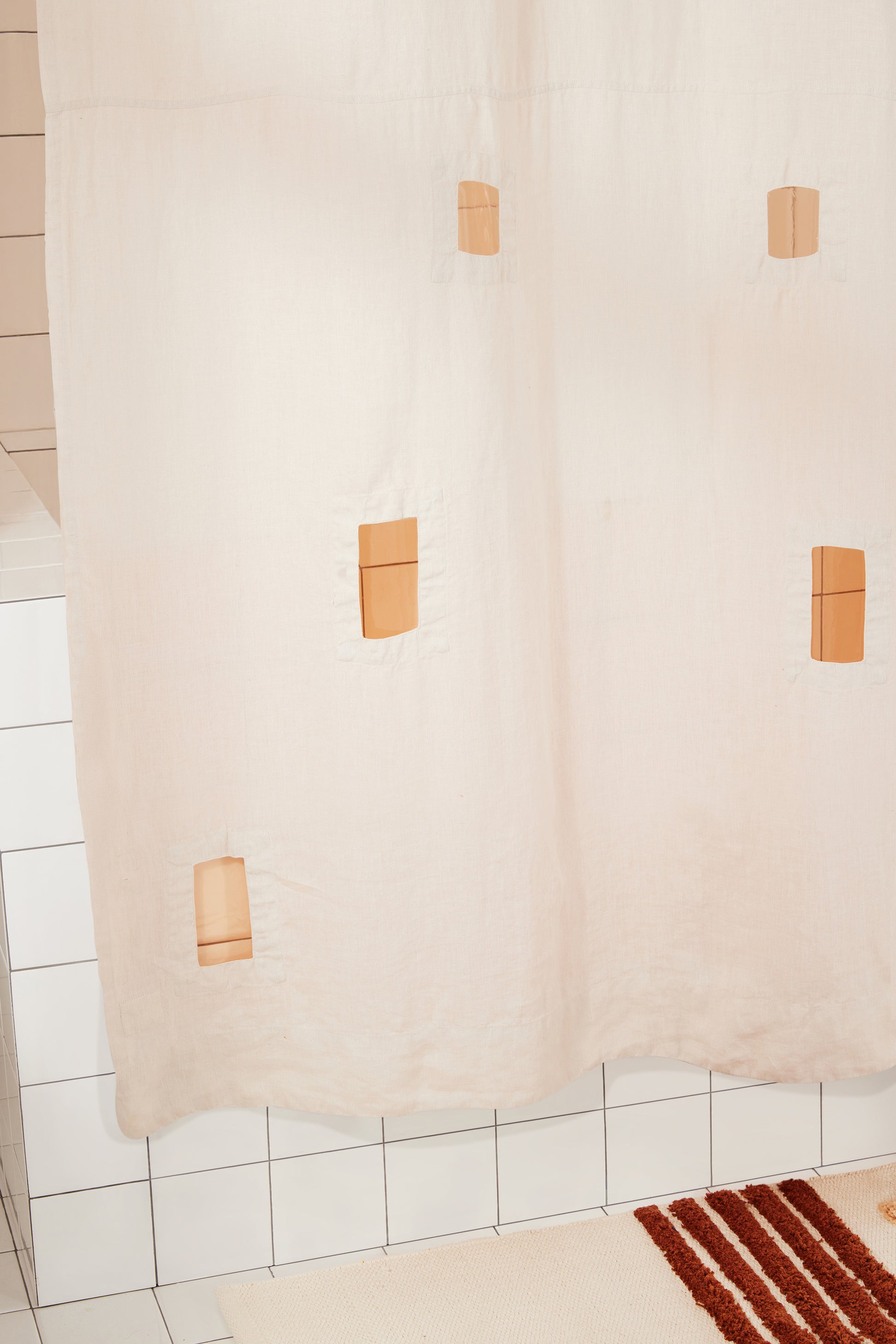 Cream shower curtain with cut outs in a tiled bathroom wall.
