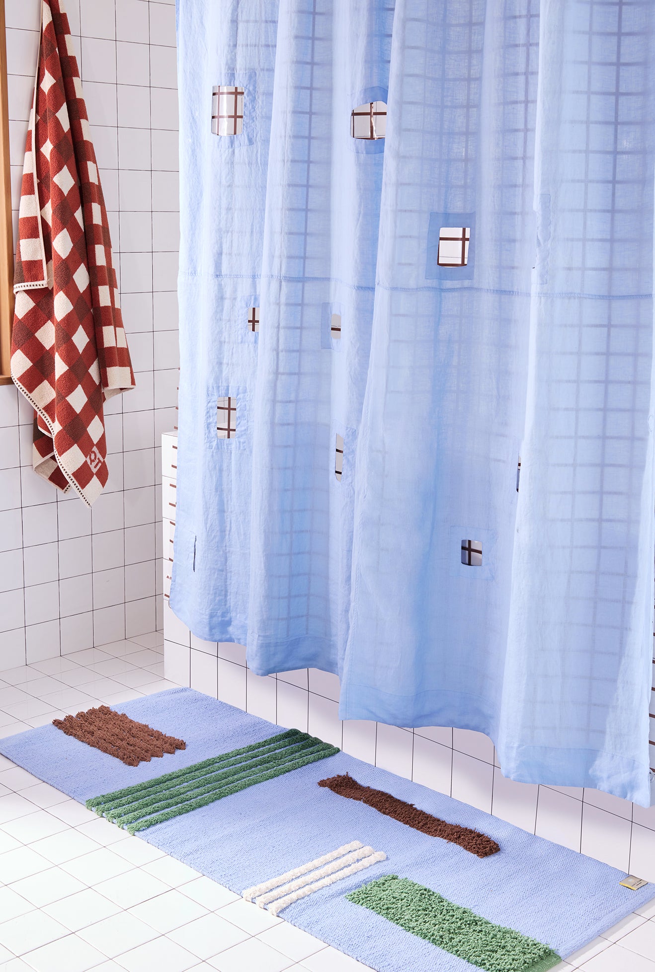 light blue shower curtain with cut outs in a white tiled bathroom and a blue patterned rug and a clay colored checkered towel.