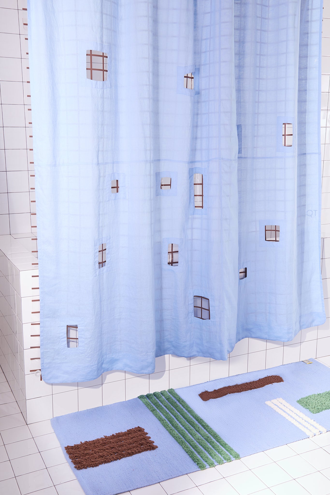 light blue shower curtain with cut outs in a white tiled bathroom and a blue patterned rug.