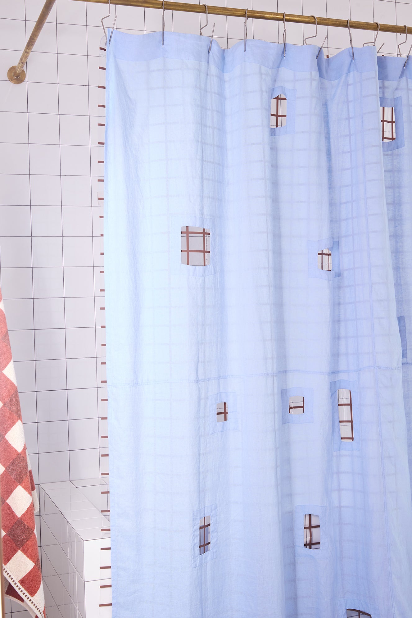 light blue shower curtain with cut outs in a white tiled bathroom.