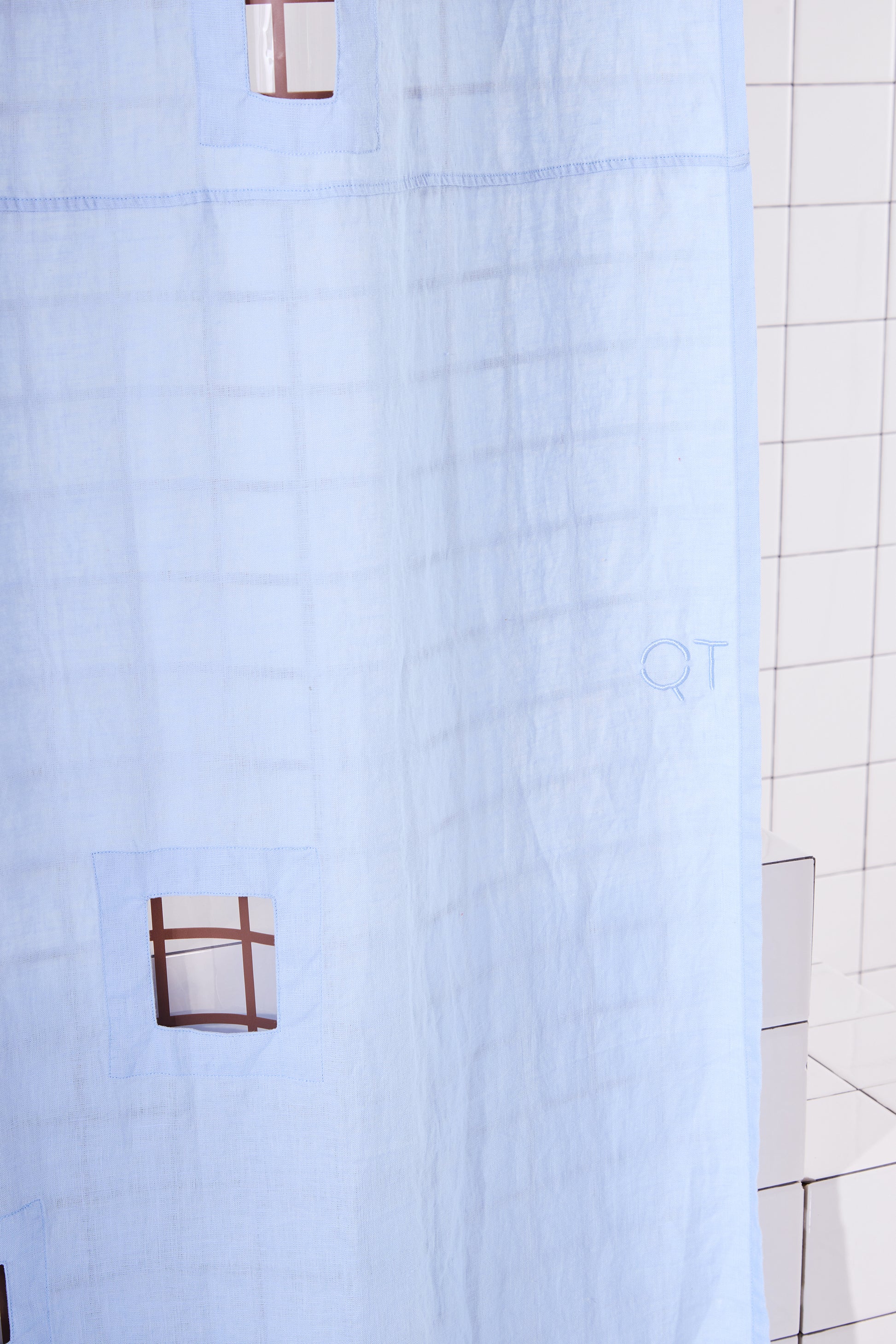 light blue shower curtain with cut outs in a white tiled bathroom.
