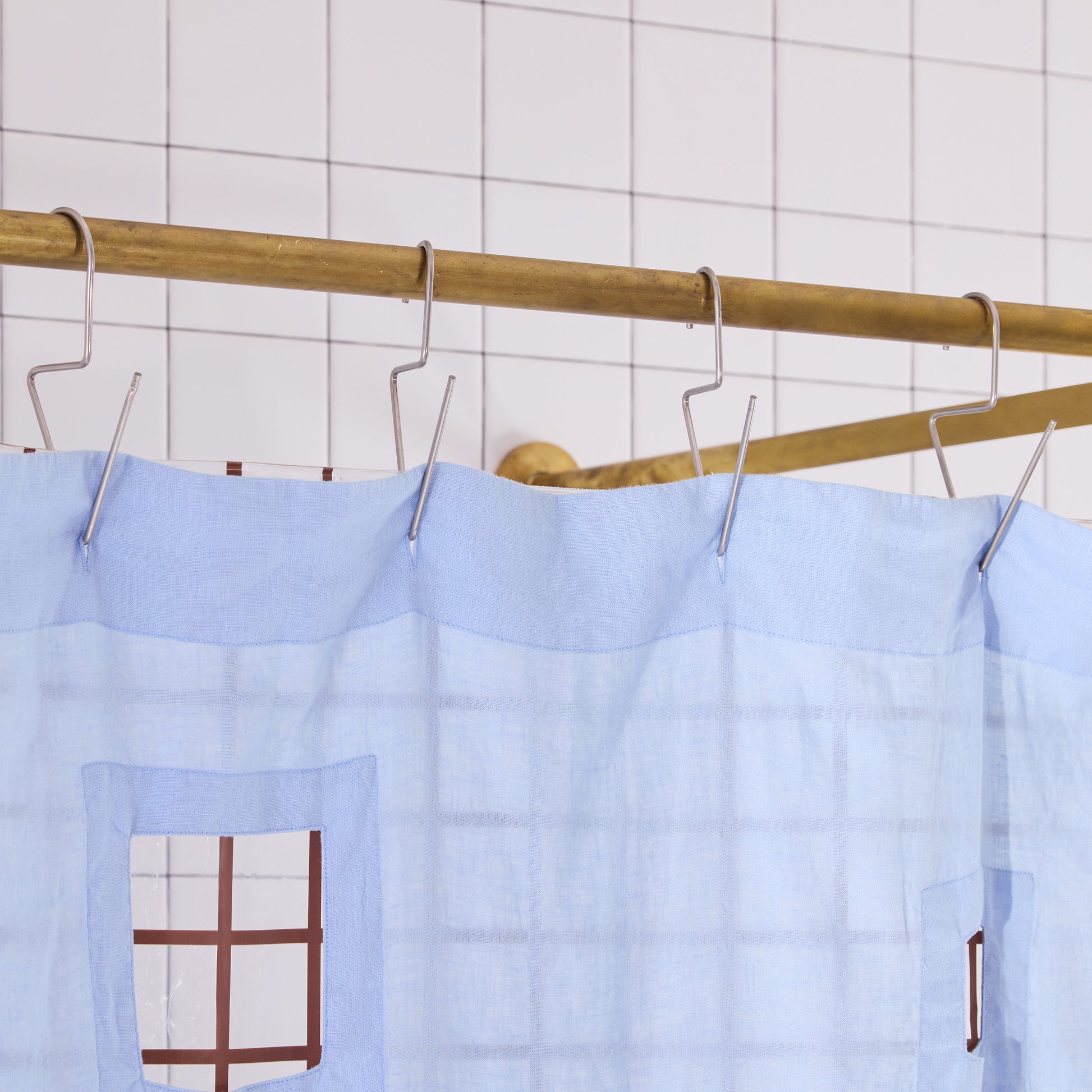 light blue shower curtain with cut outs in a white tiled bathroom.