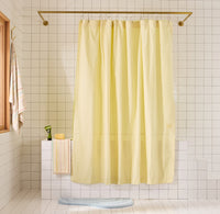 Yellow shower curtain hanging on a gold rod in a bathroom with tiled walls.