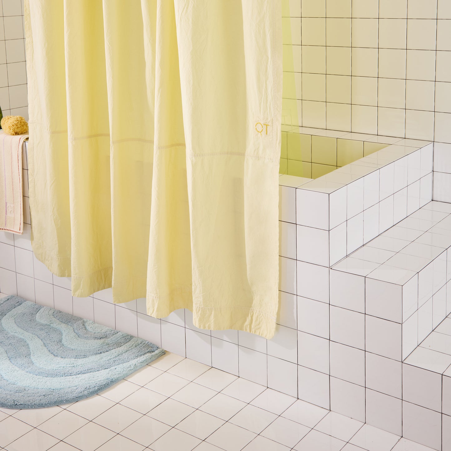 Yellow shower curtain in a bathroom with tiled walls and a rug on the floor.