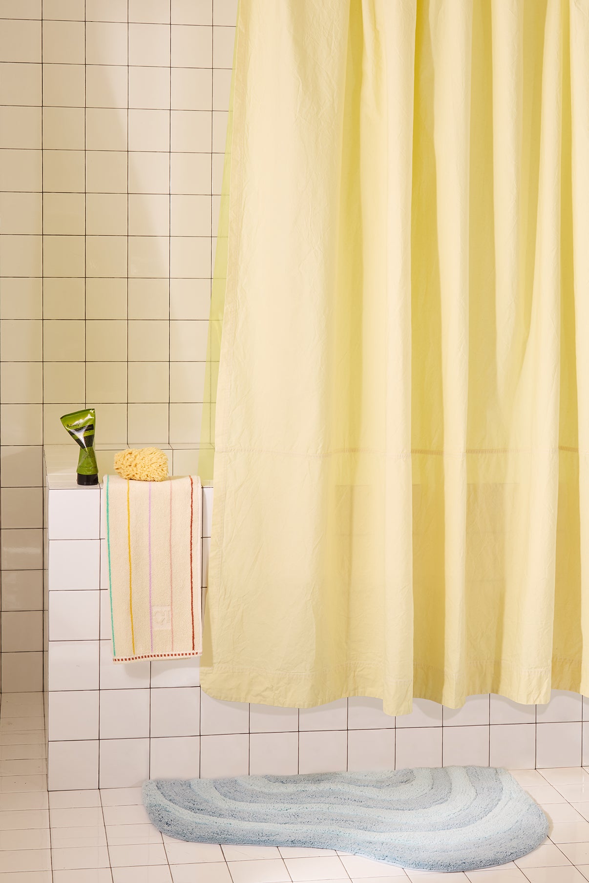 Yellow shower curtain in a bathroom with tiled walls and a bath mat on the floor.
