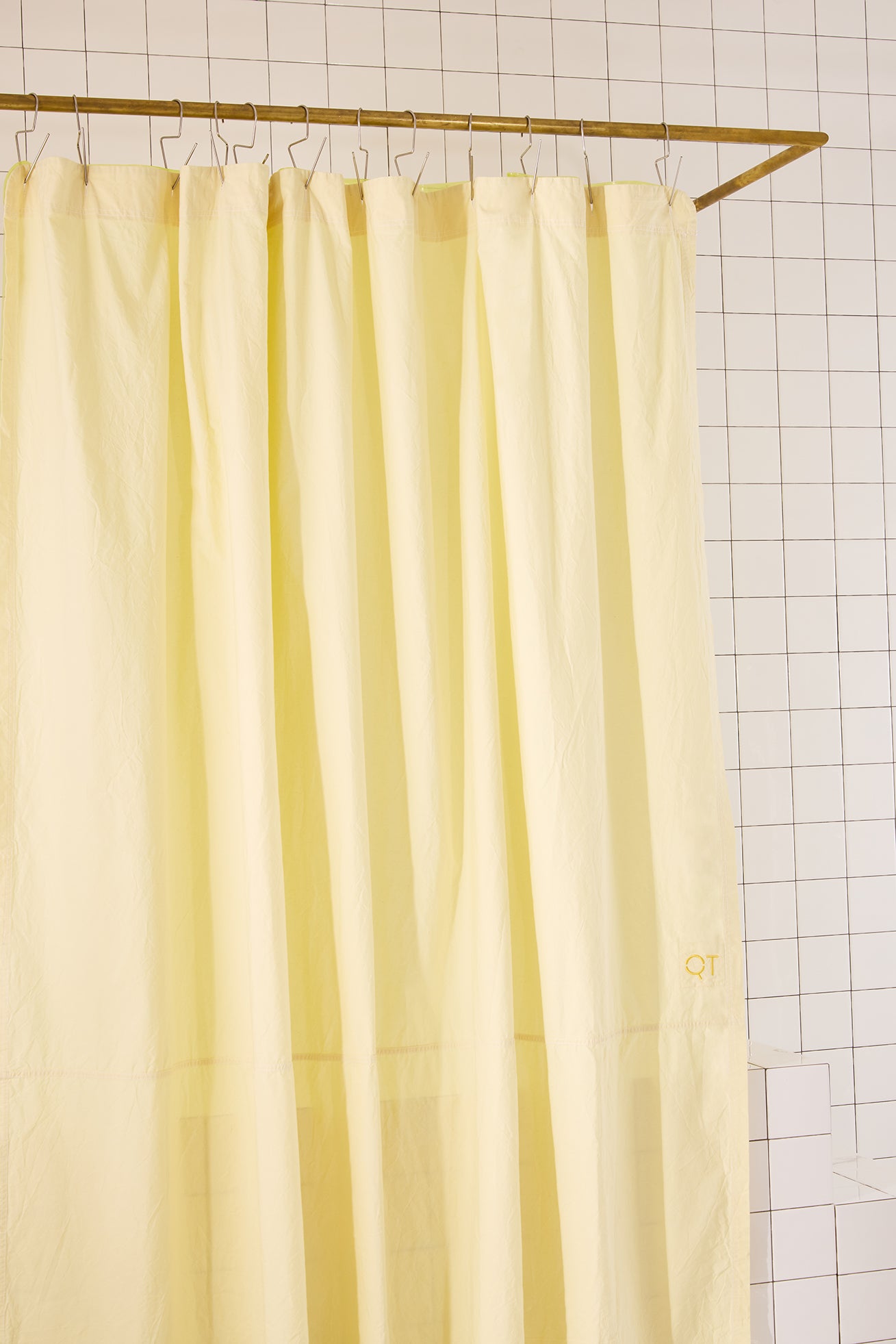 Yellow shower curtain hanging on a rod against a tiled bathroom wall.