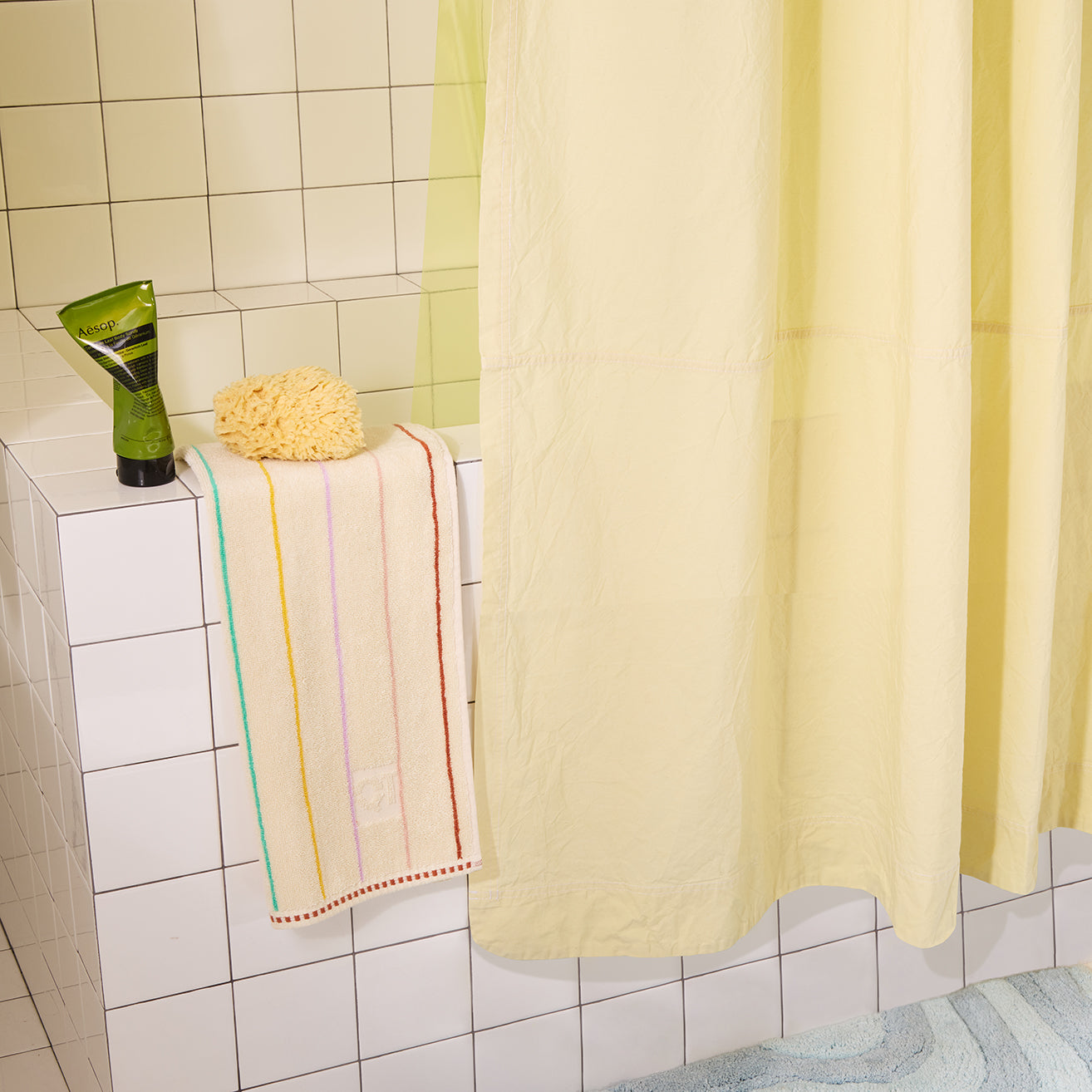 Bathroom with a yellow shower curtain, striped towel, and green bottle on a tiled shelf.