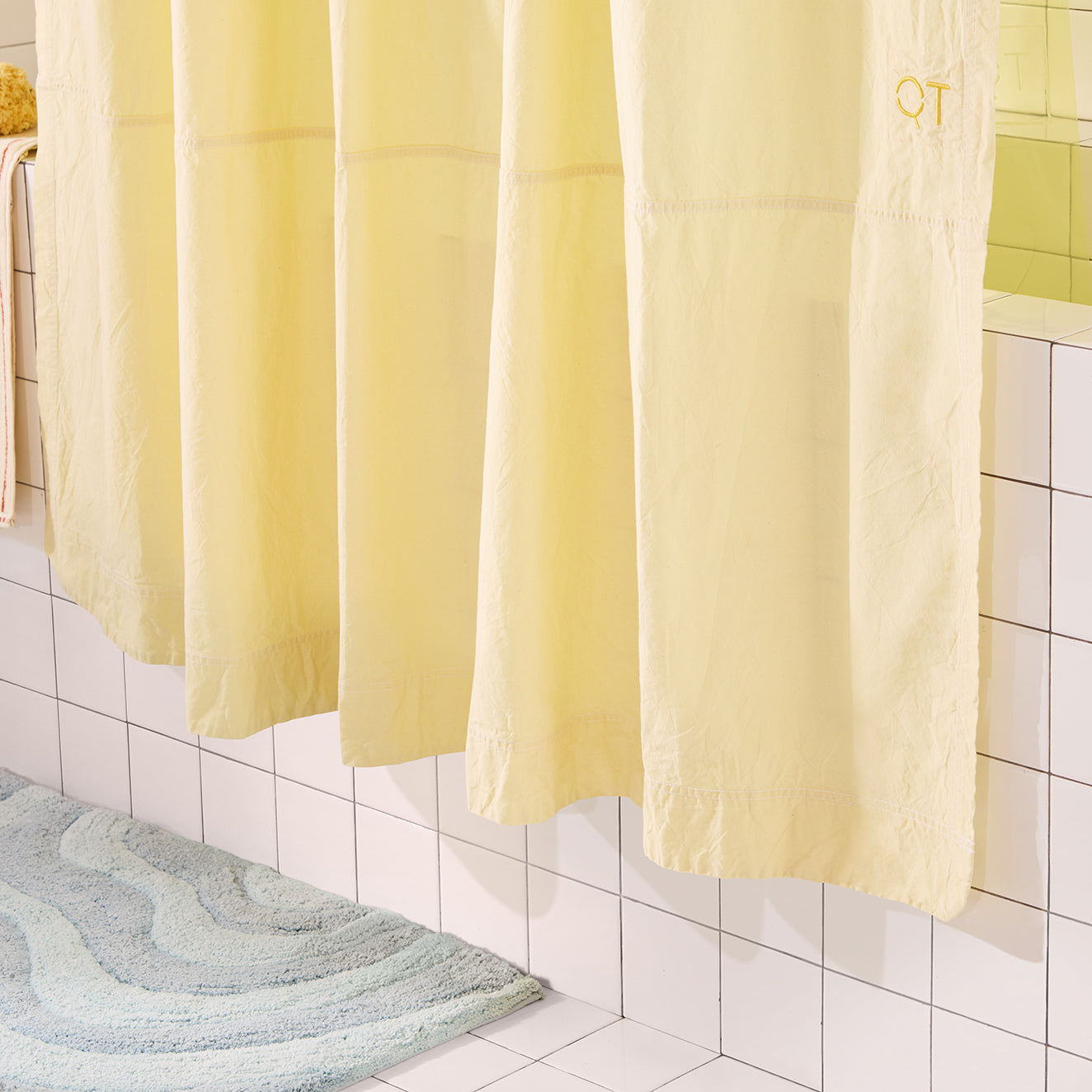 Yellow shower curtain in a bathroom with tiled walls and a green bath mat on the floor.