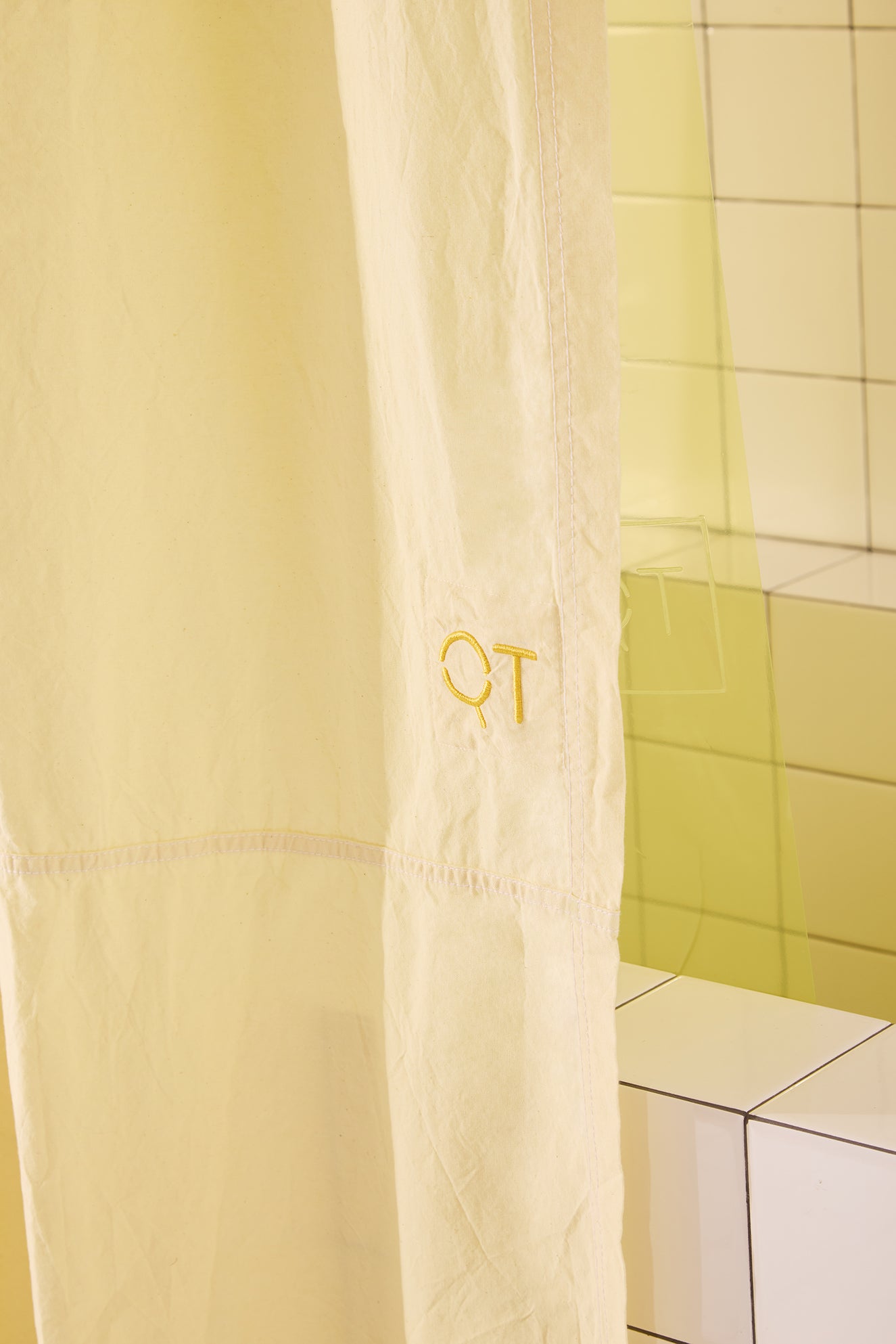 Yellow shower curtain with 'QT' logo on a tiled bathroom wall