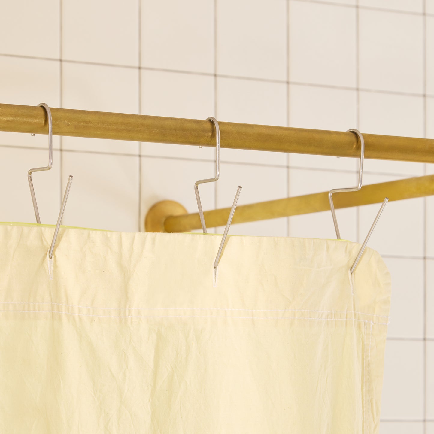 Yellow shower curtain with gold rod and silver hooks against a tiled wall.