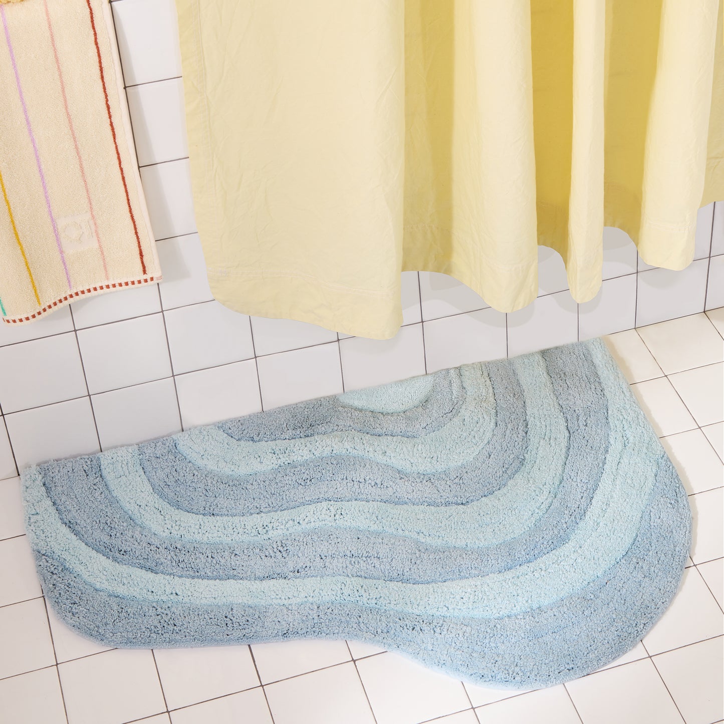 Blue curvy striped bath mat on a tiled bathroom floor with a yellow shower curtain.