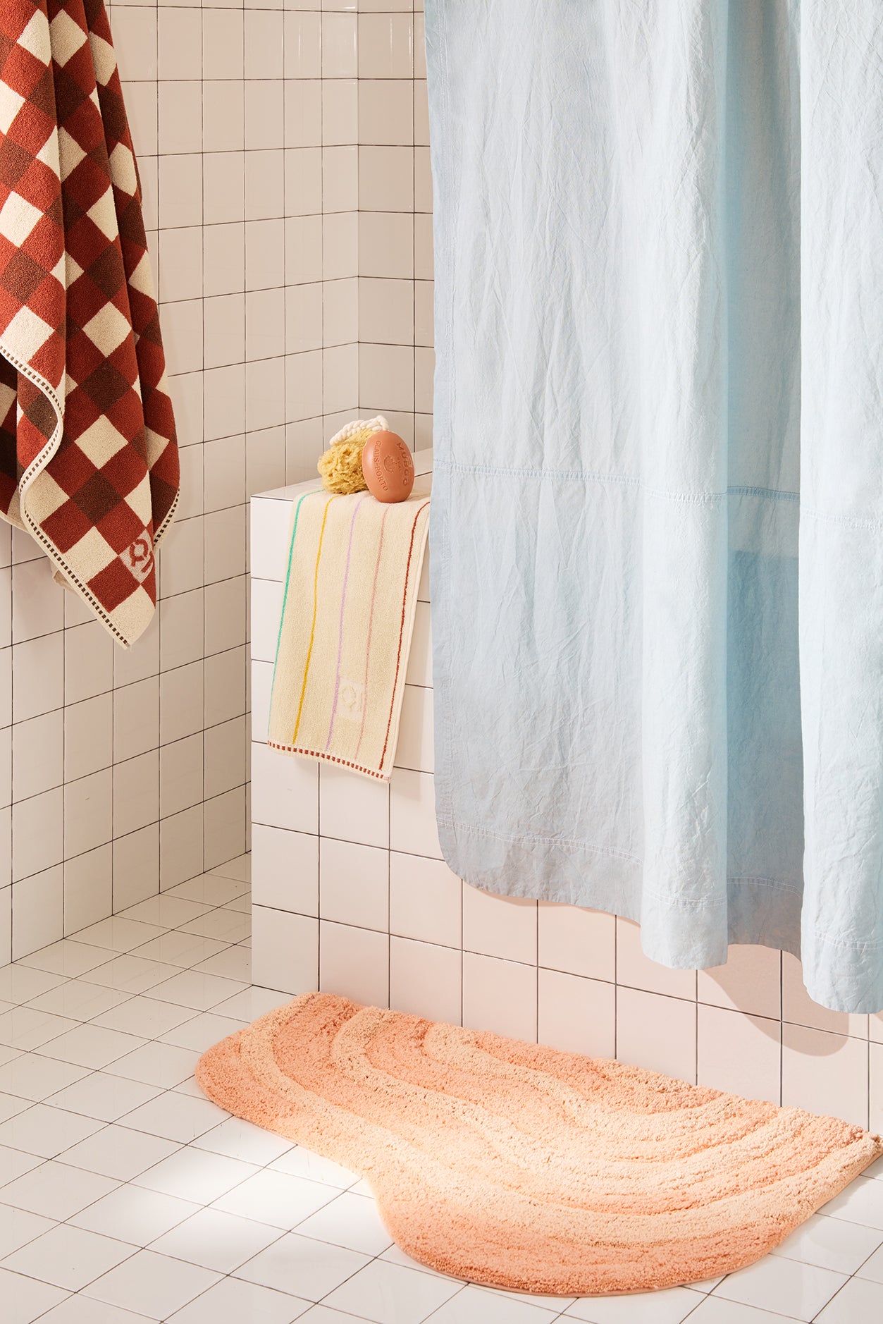 Bathroom with a peach bath mat, shower curtain, and towels on a tiled floor.