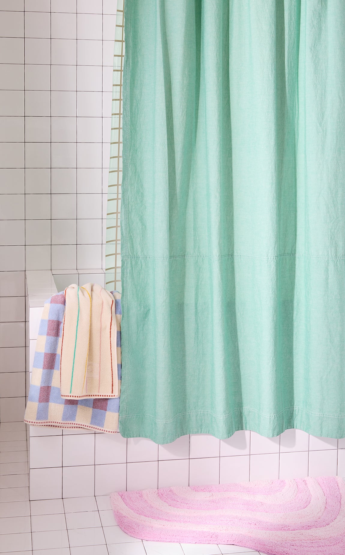 Green shower curtain with a checkered towel on a tiled bathroom wall.