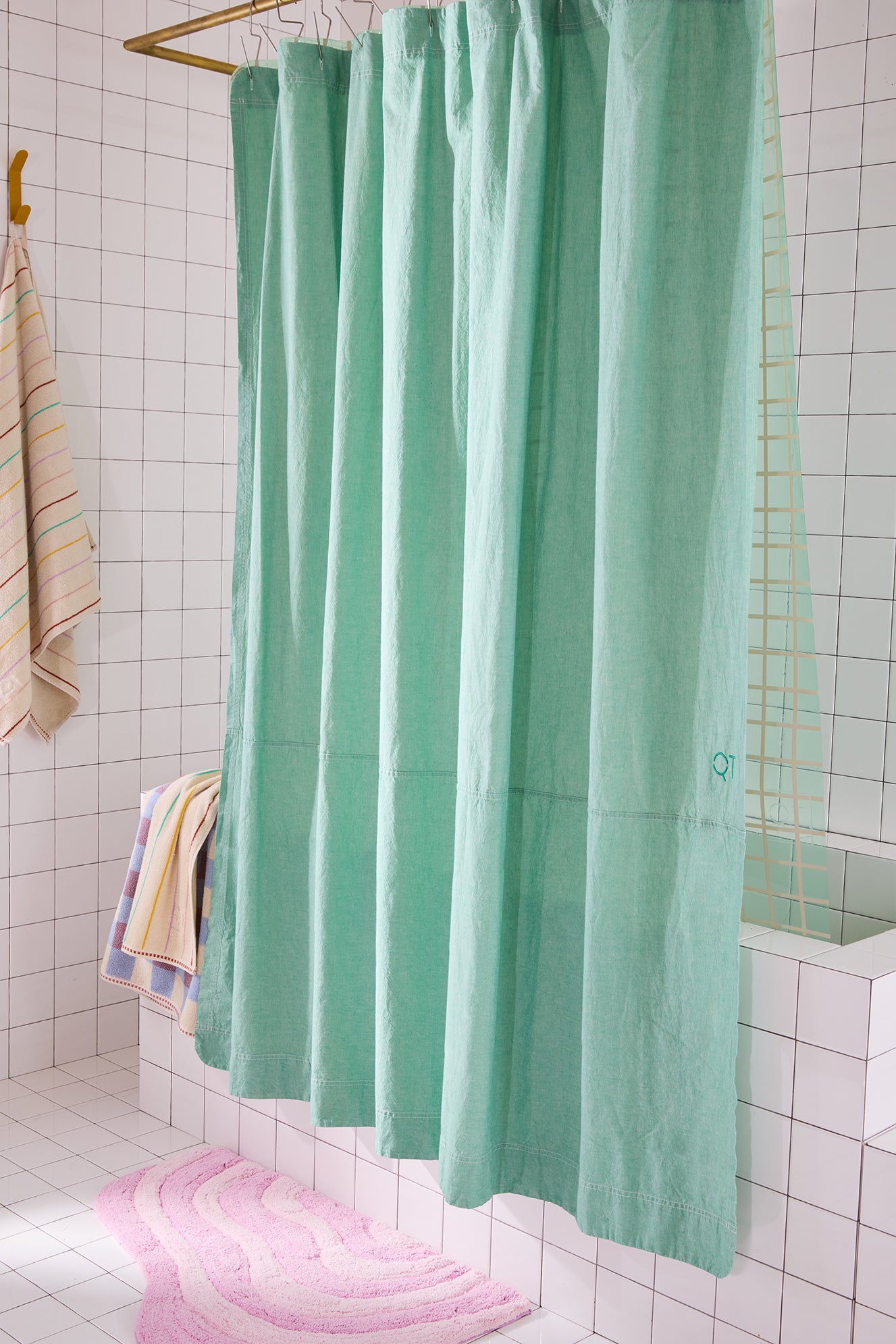 Green shower curtain in a bathroom with tiled walls and a pink bath mat on the floor.
