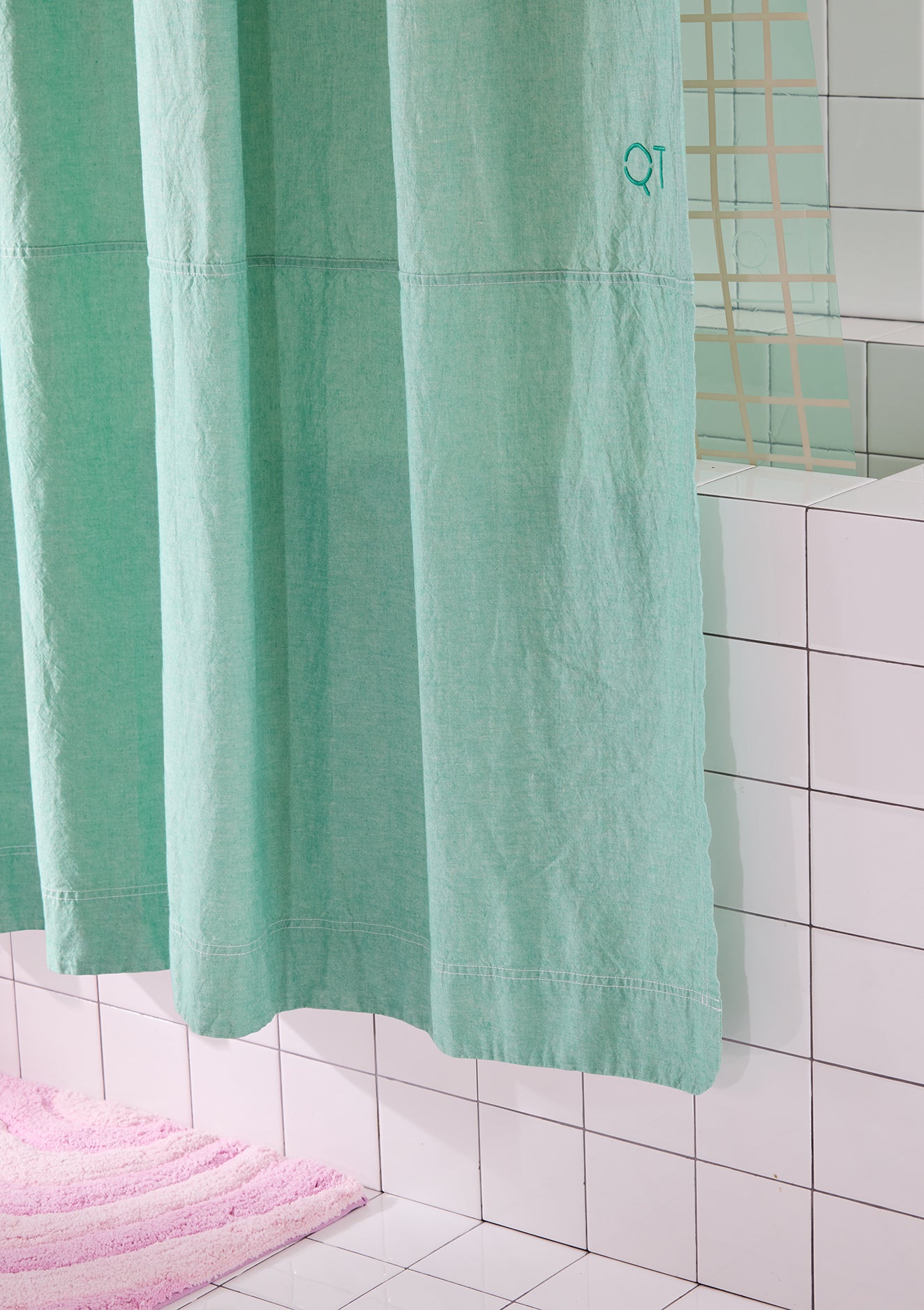 Green shower curtain in a bathroom with tiled walls and a pink bath mat.
