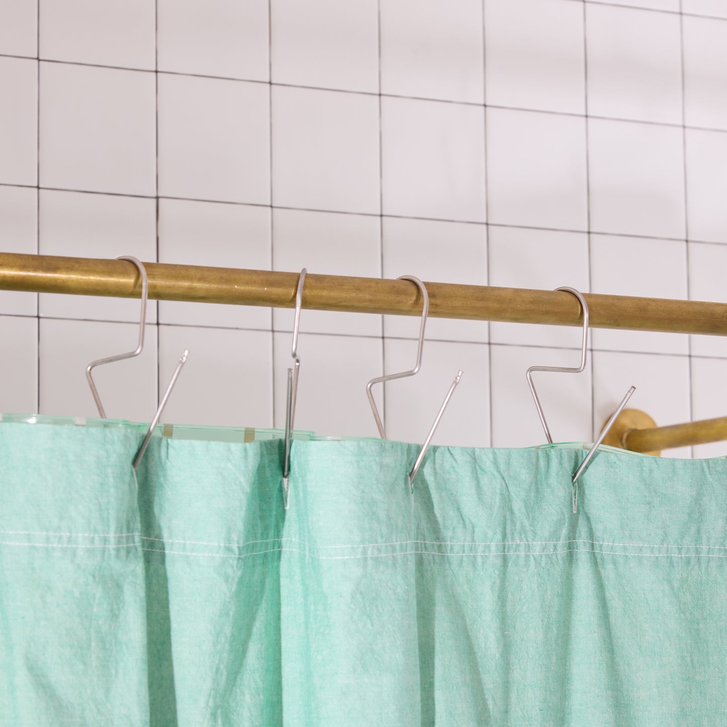 Green shower curtain with brass rod and hooks against a tiled wall