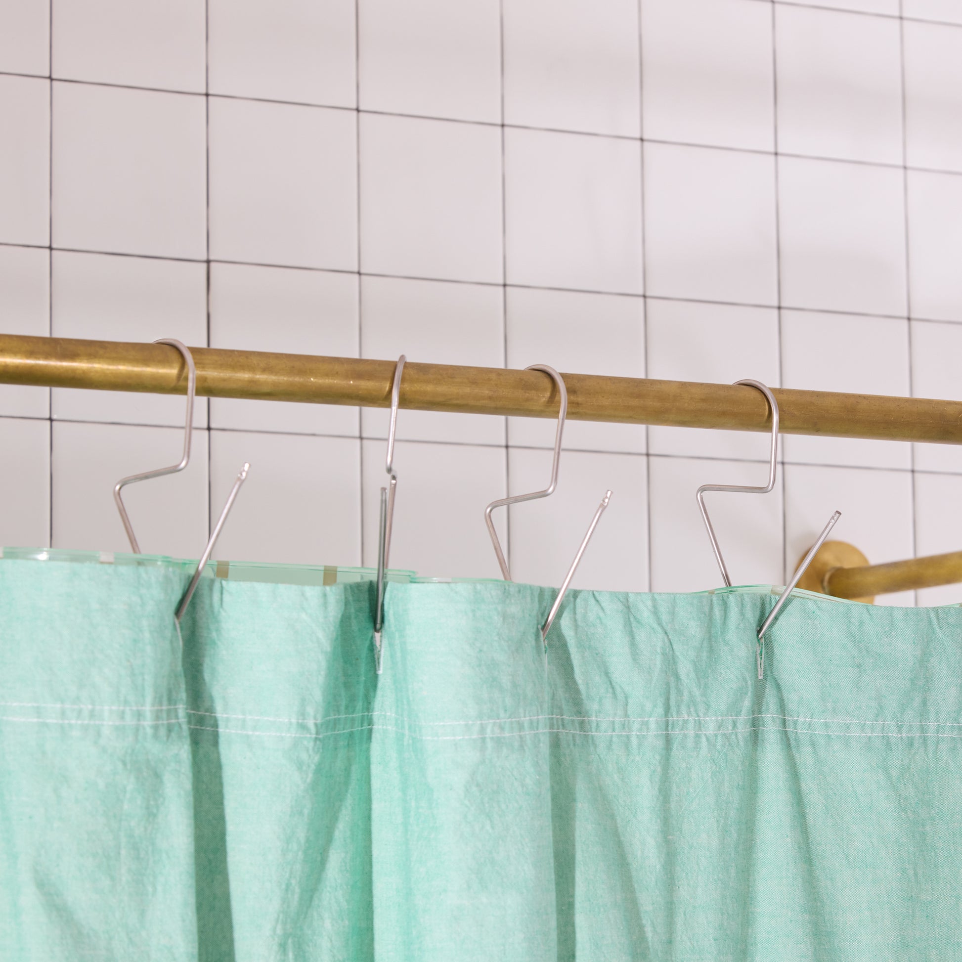 Green shower curtain with brass rod and hooks against a tiled wall