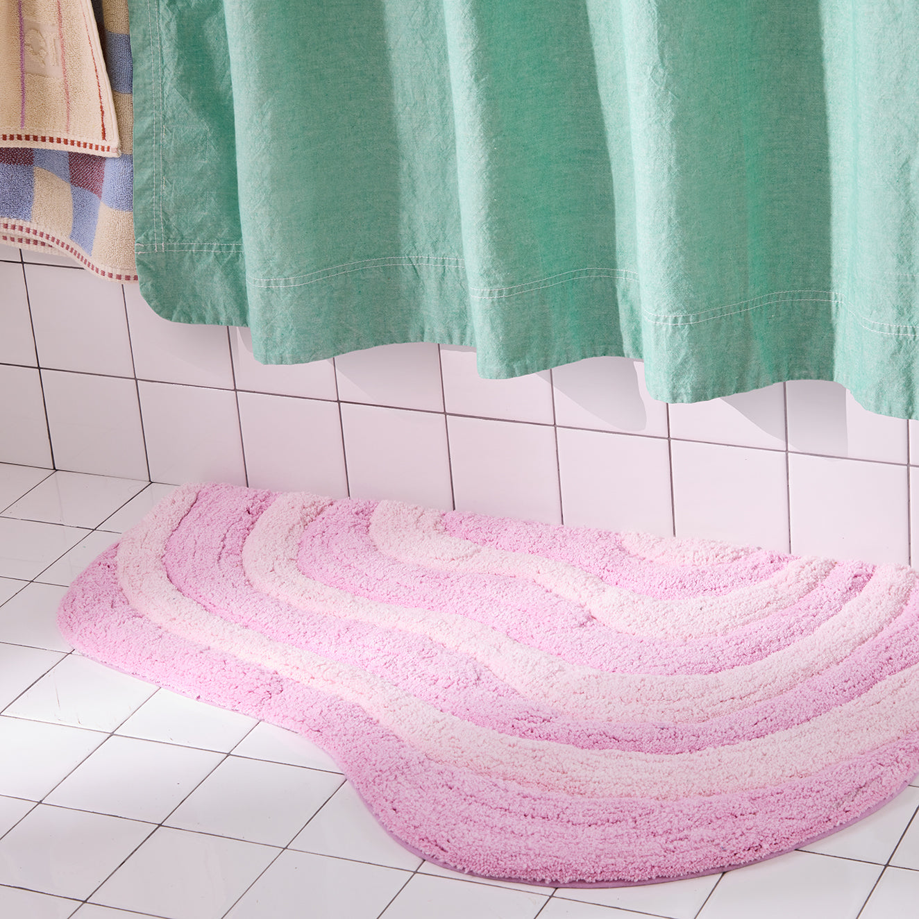 Pink wavy bath mat on a tiled bathroom floor with a green shower curtain.