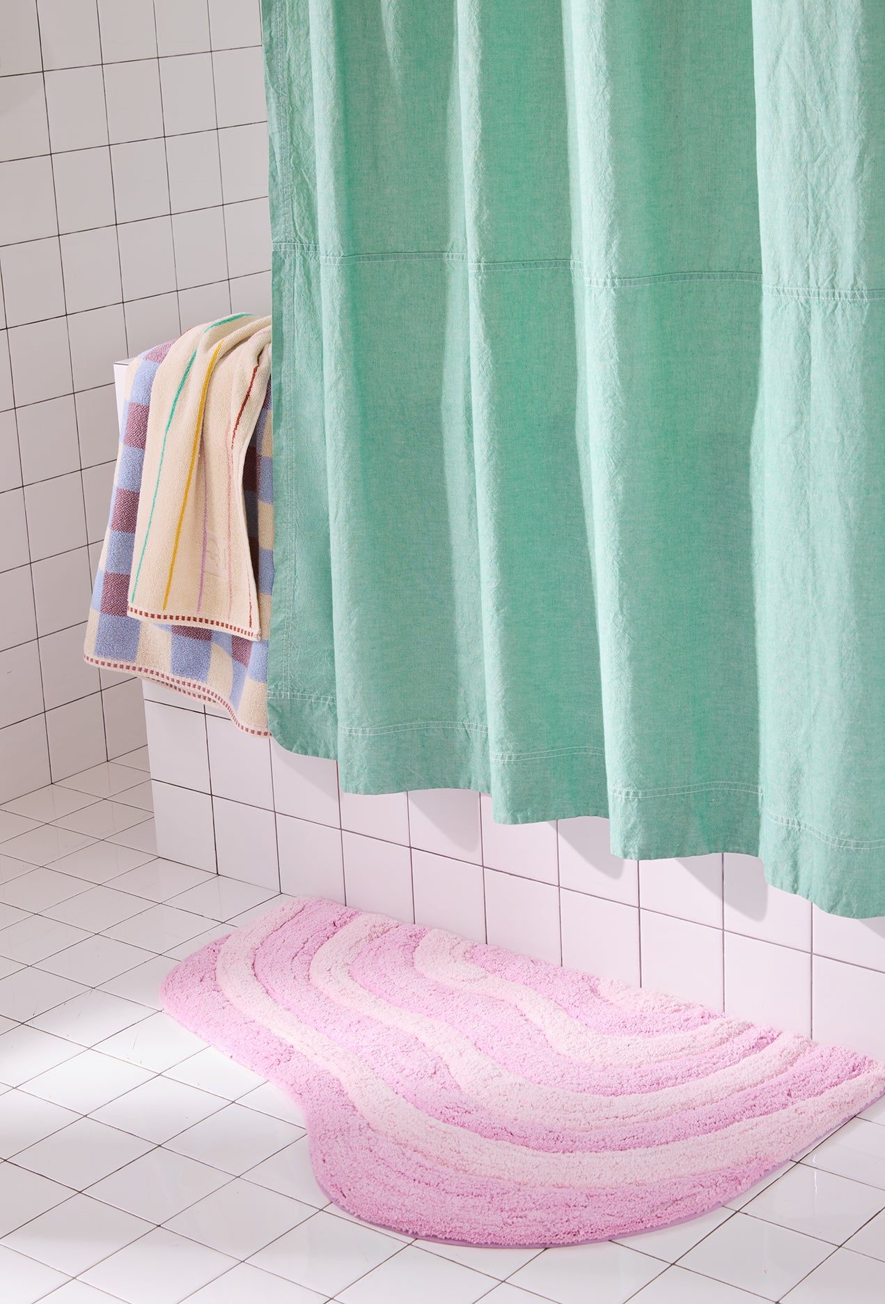 Pink bath mat on a tiled bathroom floor with a green shower curtain.