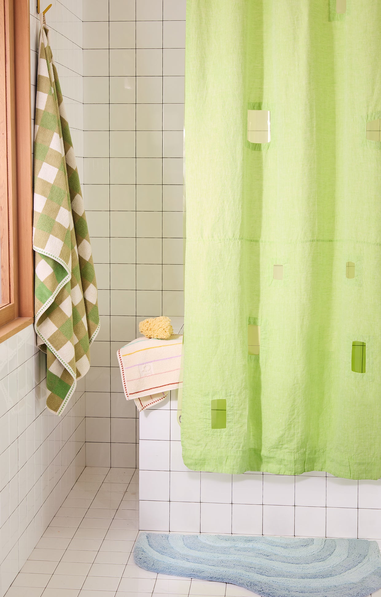 bright green shower curtain in a white tiled bathroom with green checker towel and blue rug