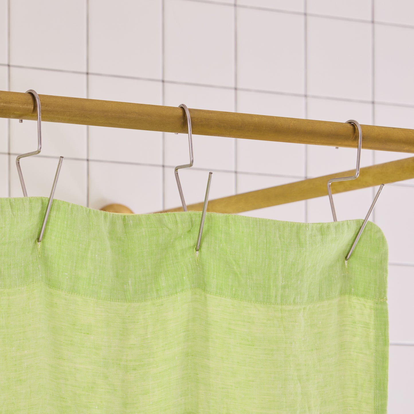 green curtain hem with silver hooks on brass rod. 