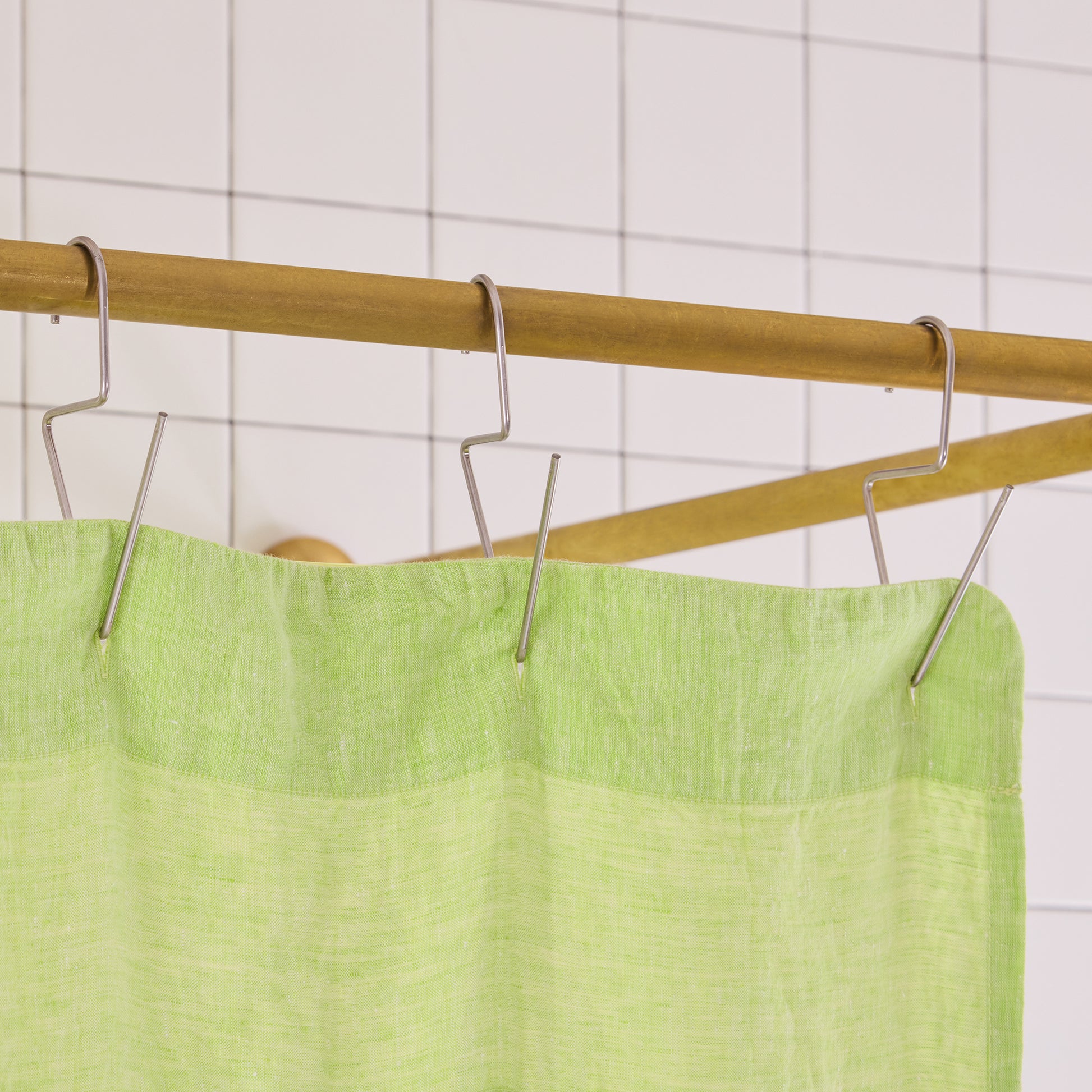 green curtain hem with silver hooks on brass rod. 