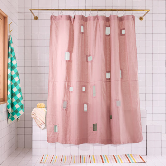 Pink shower curtain with geometric cut-outs in a white tiled bathroom.