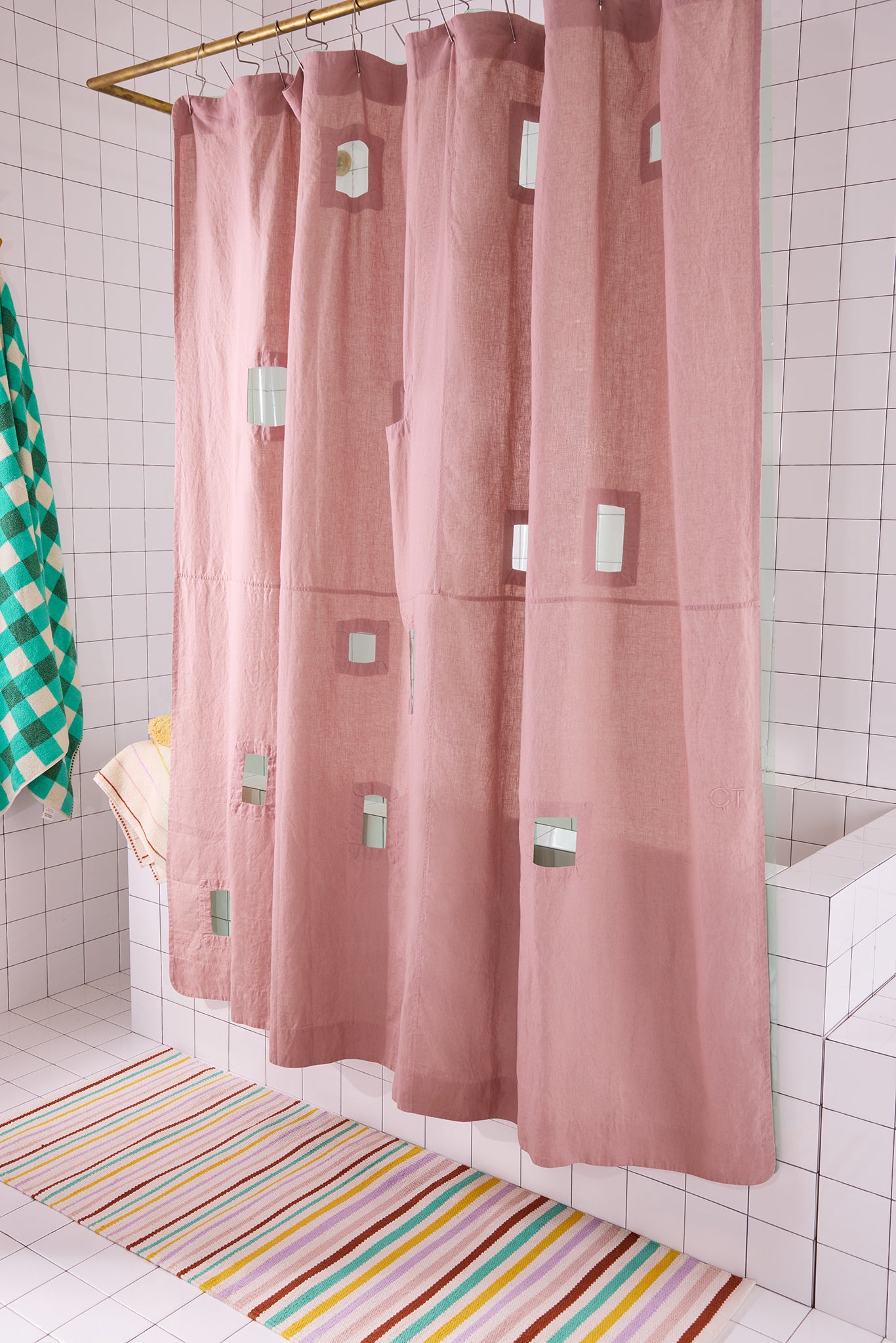 Pink shower curtain with silver hooks in a bathroom with a striped rug.