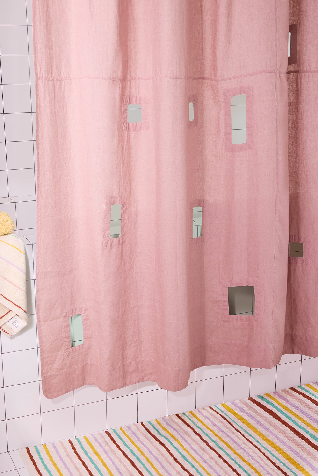 Pink shower curtain with geometric cutouts in a bathroom with tiled walls and a colorful rug.