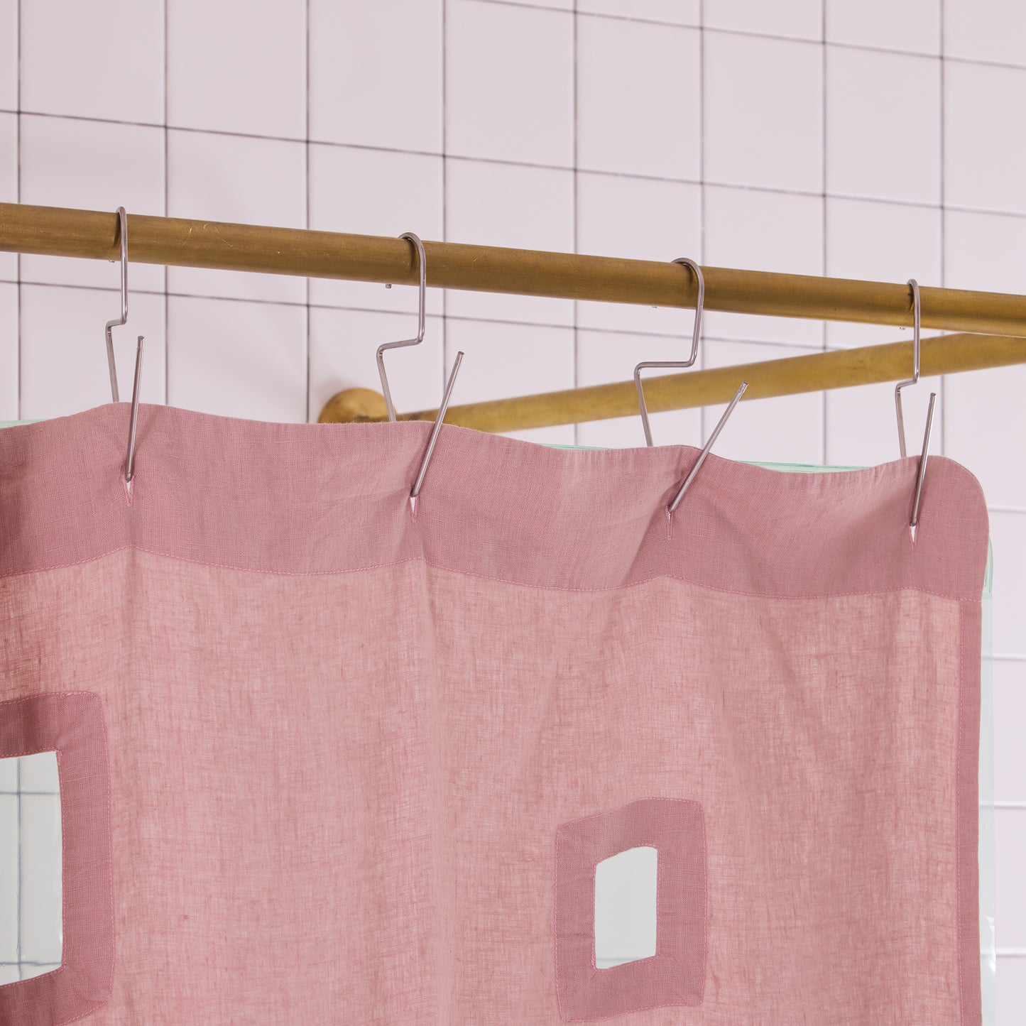 Pink shower curtain with cutouts hanging on a gold rod against a tiled wall.