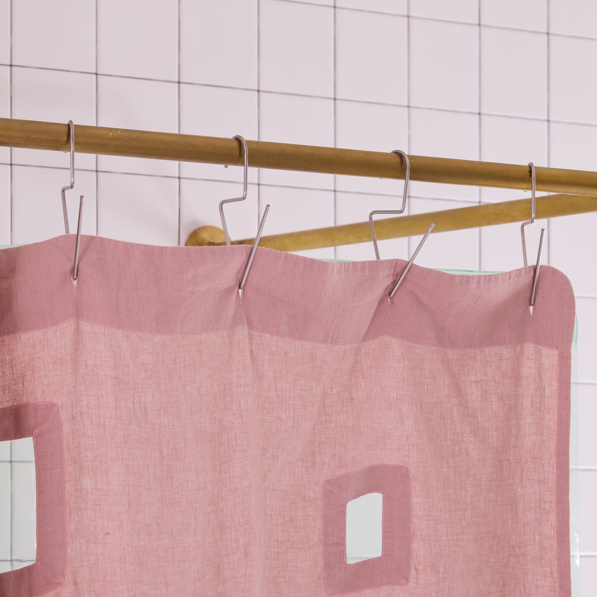Pink shower curtain with cutouts hanging on a gold rod against a tiled wall.