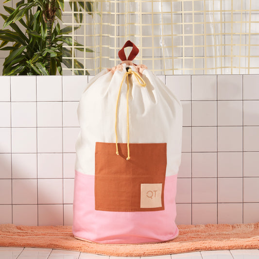 pink, cream and clay colored laundry backpack on peach rug 