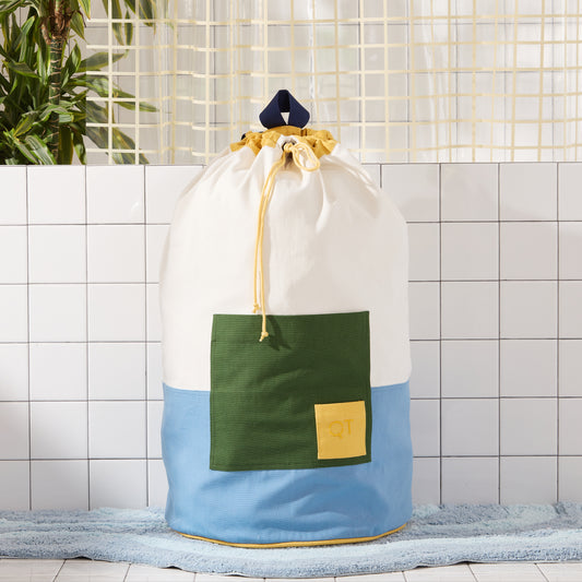 colorblocked blue laundry bag with green pocket on blue rug.