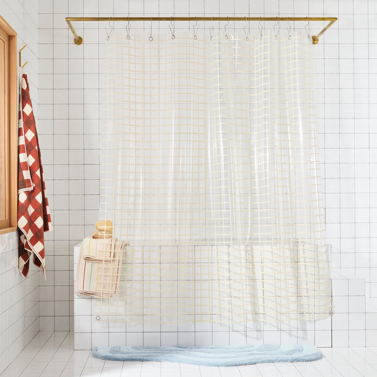 Clear shower curtain with cream grid print on a gold rod in a bathroom setting