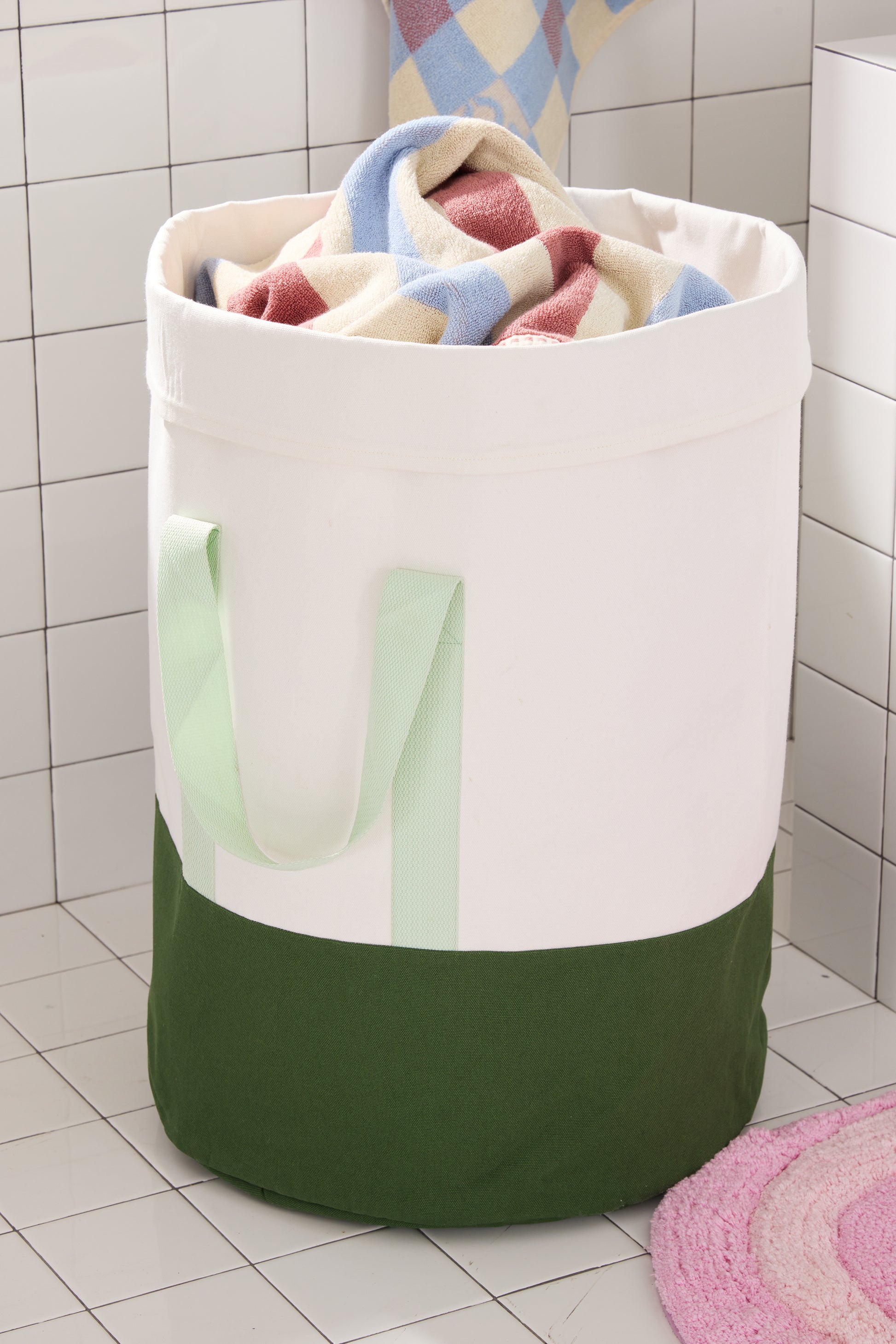 green and cream laundry hamper in white tiled bathroom