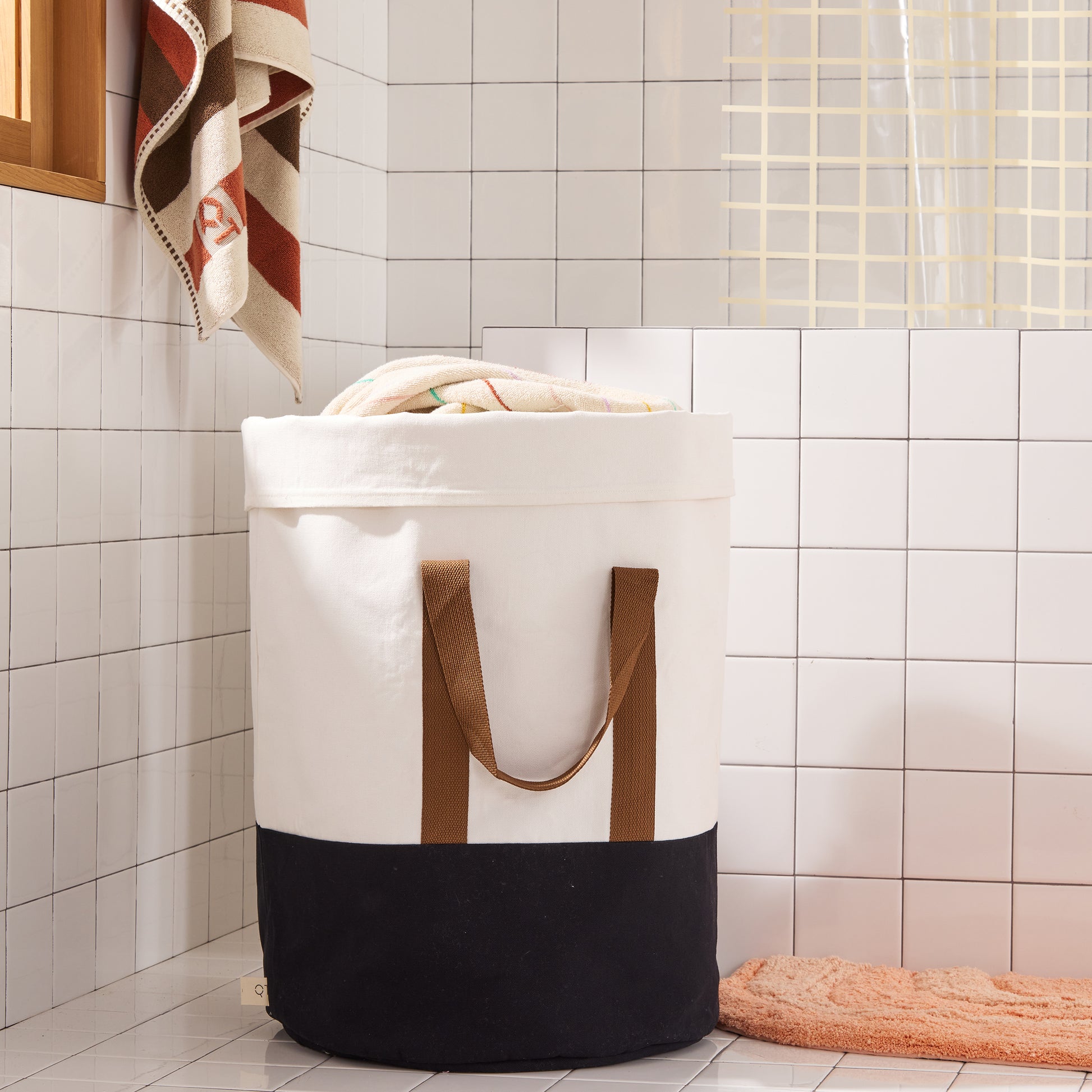 laundry hamper wtih black bottom and brown straps in a tiled bathroom. 