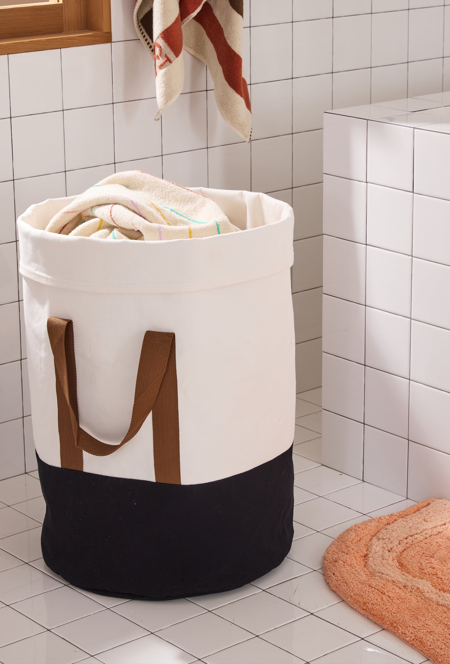 cream hamper with lack bottom and brown straps in a tiled bathroom. 