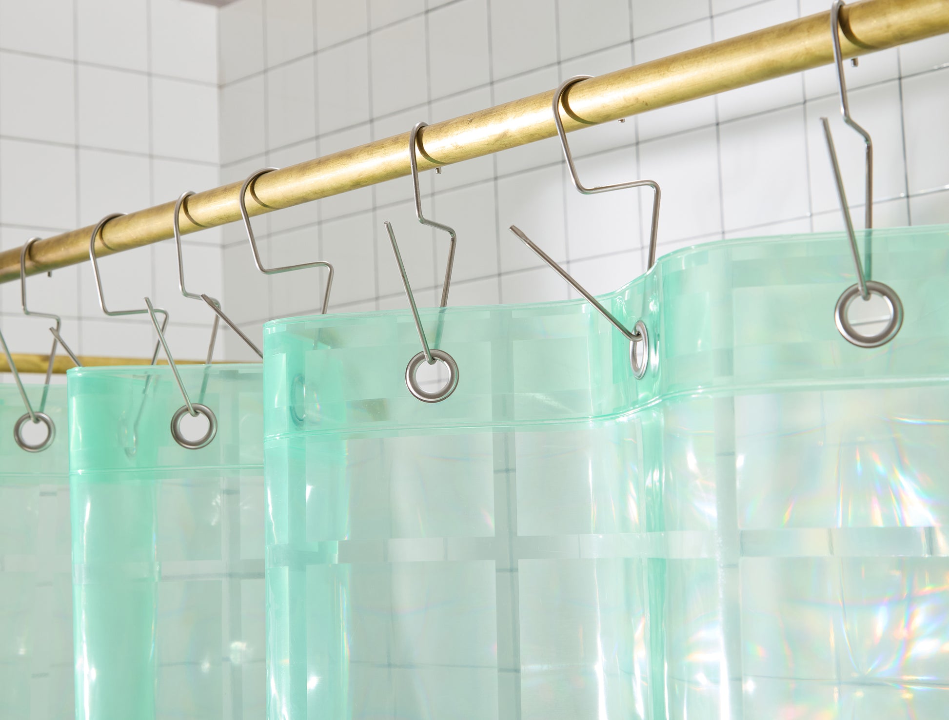 top hem of mint colored shower curtain with silver grommets hangs on brass rod.